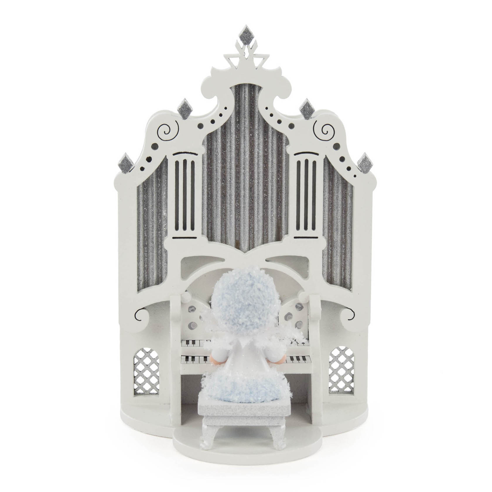 Eine kleine weiße Puppe namens Schneeflöckchen sitzt auf einem Hocker vor einer detailreichen weißen Orgel mit silbernen Verzierungen.