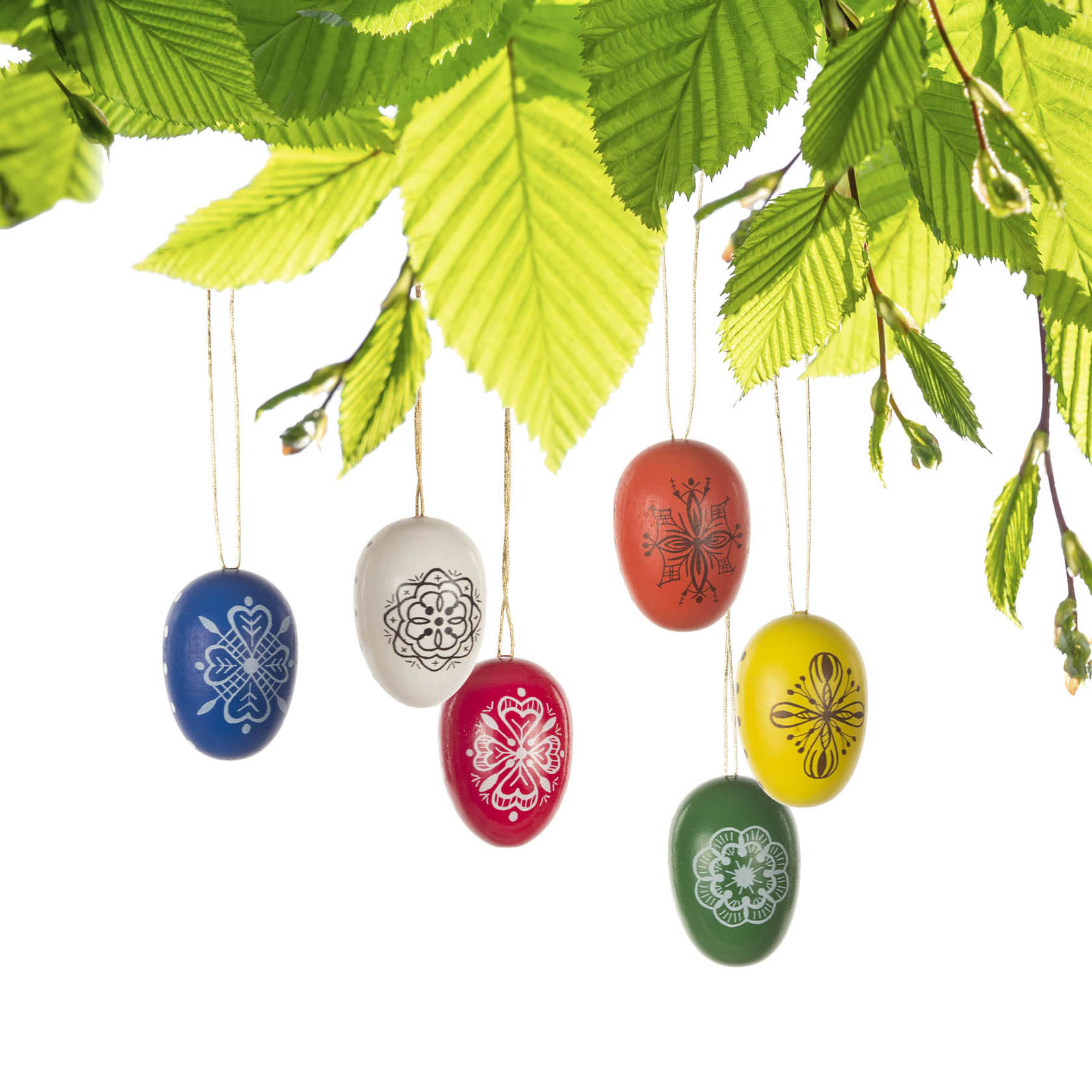 Sechs bunte Ostereier mit aufgemalten traditionellen Mustern hängen an Fäden von einem Ast. Die Eier sind in den Farben Blau, Weiß, Rot, Orange, Gelb und Grün bemalt.