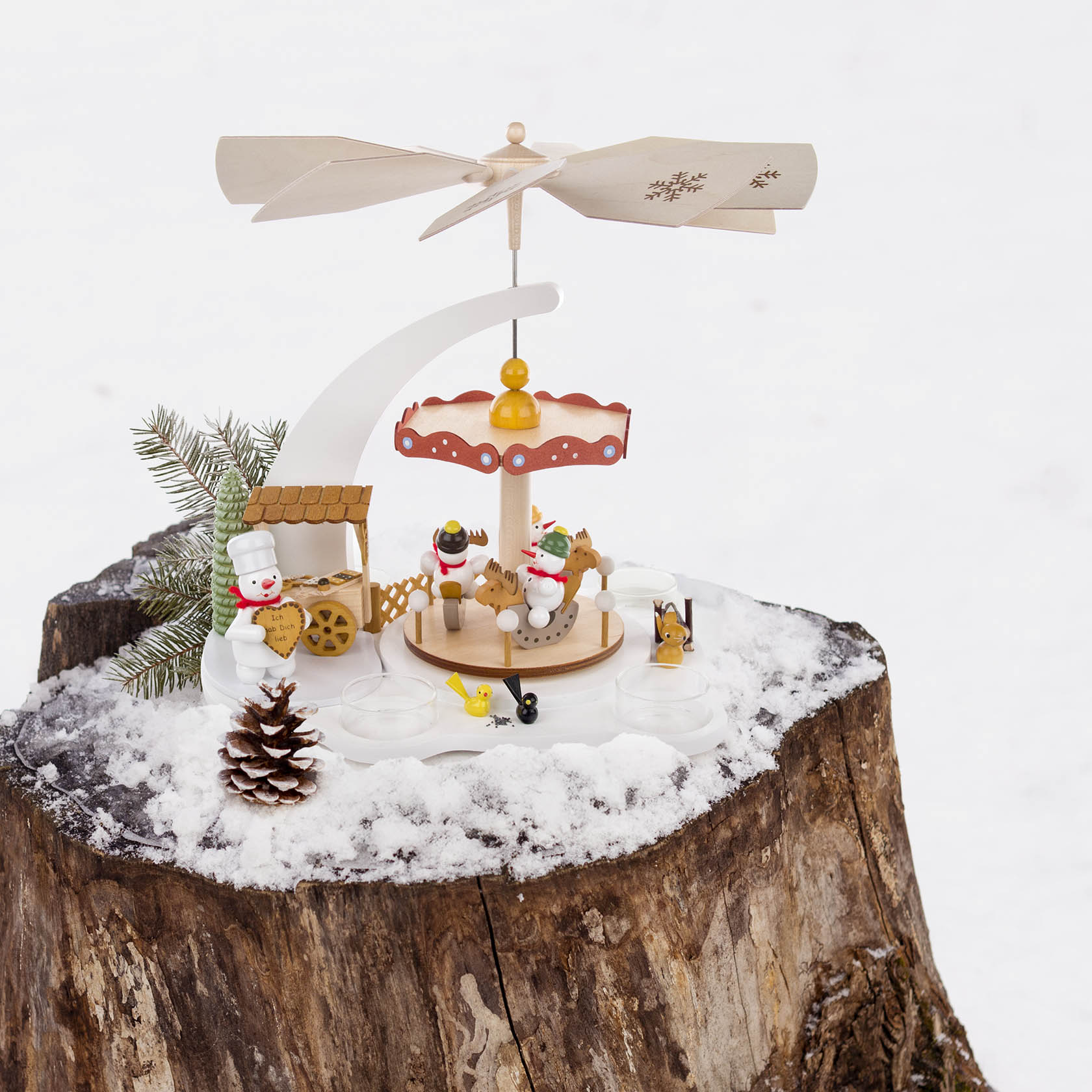 Weiße Pyramide in Form eines Schneemann-Karussells mit Platz für Teelichter, dekoriert mit Schneemännern, einem Hund und einem Vogel auf einem verschneiten Baumstumpf.