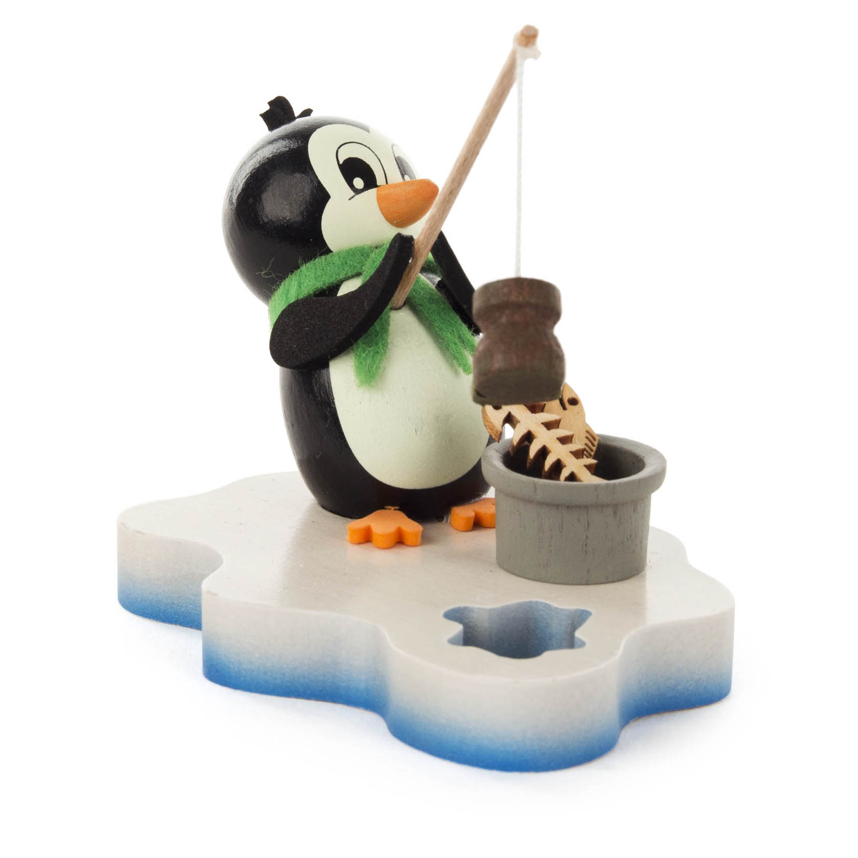 Holzfigur eines Pinguins mit grünem Schal angelt einen Fisch aus einem grauen Eimer, steht auf einer Eisplatte.