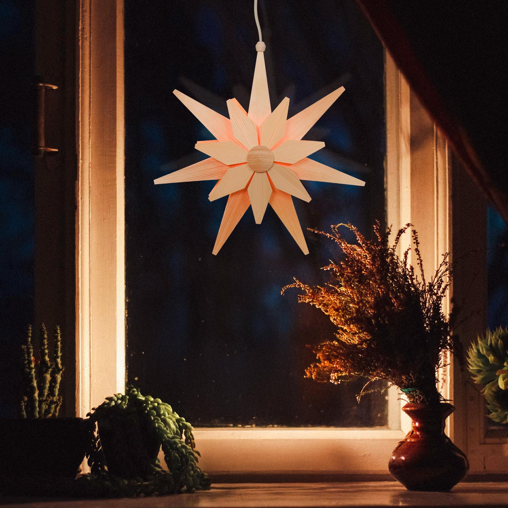 Im Fenster hängt ein doppelt geschichteter Weihnachtsstern mit natürlichem Holz-Look und elektrischer Beleuchtung.