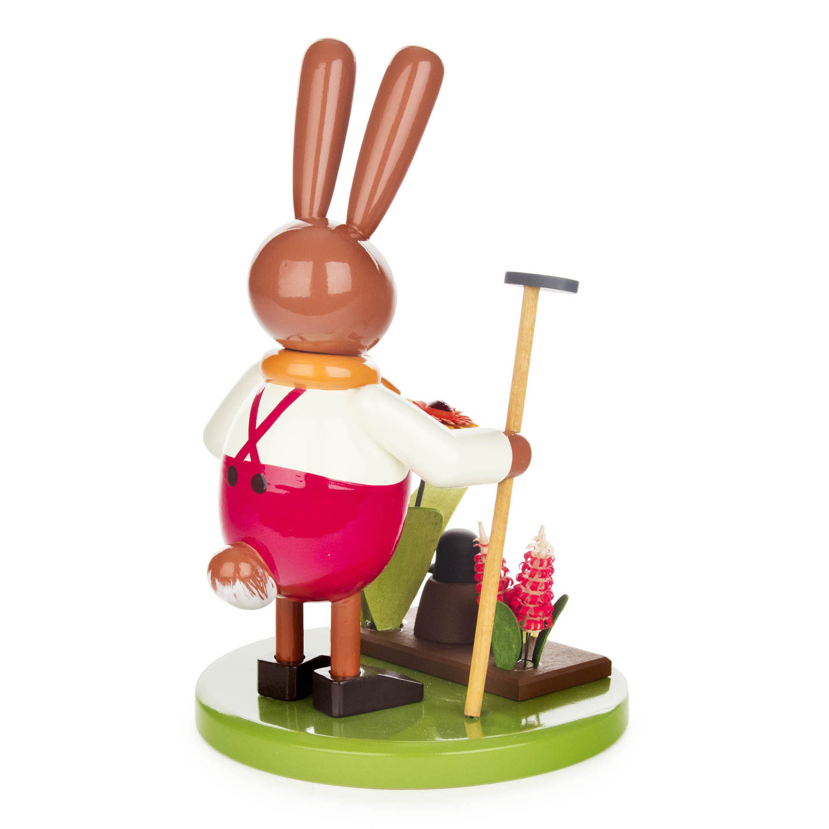 Holzfigur eines Hasen mit roten Hosen und einer Hacke, neben einem Maulwurf in einem Beet mit Blumen.