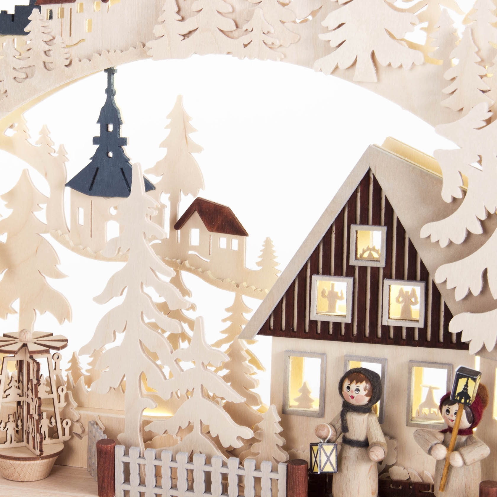 Ein Schwibbogen aus Holz zeigt eine winterliche Szene mit einem Fachwerkhaus, in dem Lichter leuchten, und zwei Figuren mit Laternen davor.