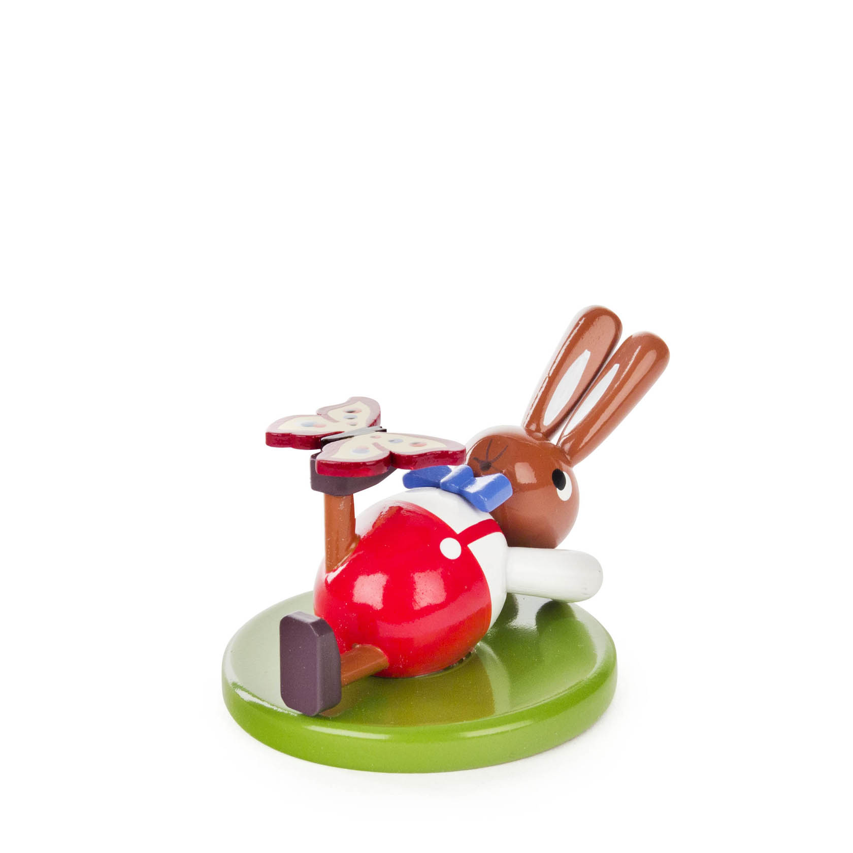 Kleine, liegende Hasenfigur mit braunen Ohren, roter Hose und blauem Hemd, ein Schmetterling sitzt auf dem Fuß. Figur ruht auf einem grünen Sockel. im Dregeno Online Shop günstig kaufen