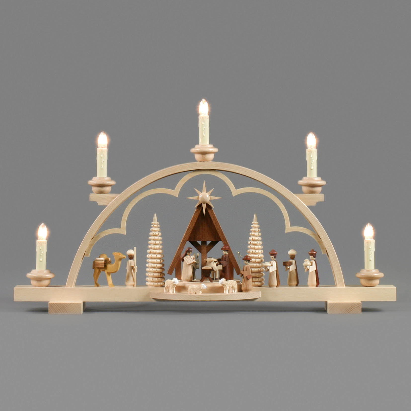 An electric lit Schwibbogen depicting the Nativity scene with a wooden arch, featuring figures of Mary, Joseph, baby Jesus, shepherds, and a camel.