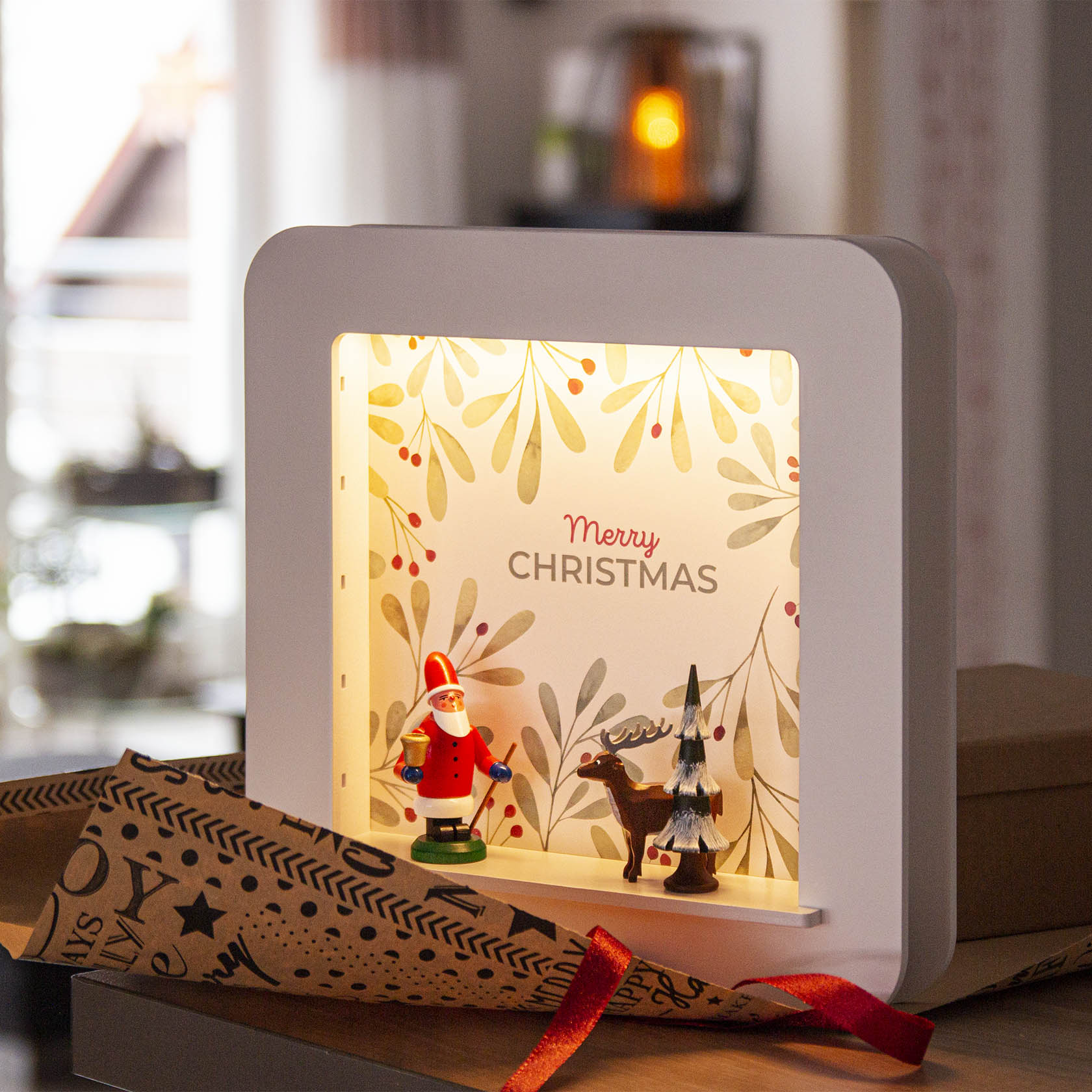 Eine leuchtende Spandose mit einer Weihnachtsdeko aus einem Weihnachtsmann, einem Hirsch und einem kleinen Weihnachtsbaum. Im Hintergrund steht 'Merry Christmas'.