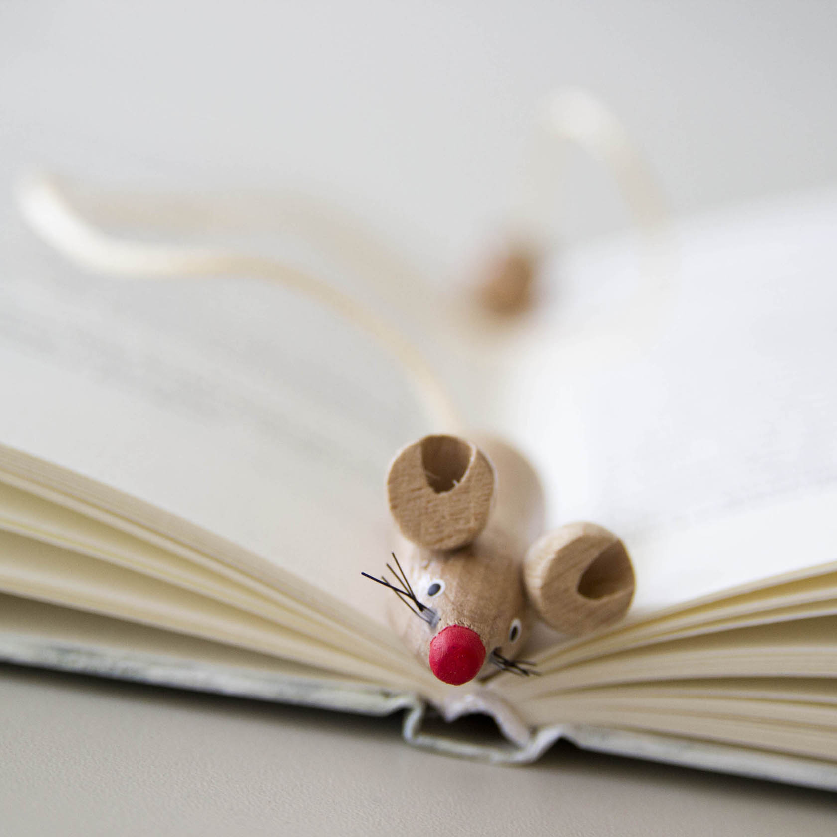 Eine hölzerne Figur einer Maus mit roten Nase und Schnurrhaaren liegt auf einem geöffneten Buch.