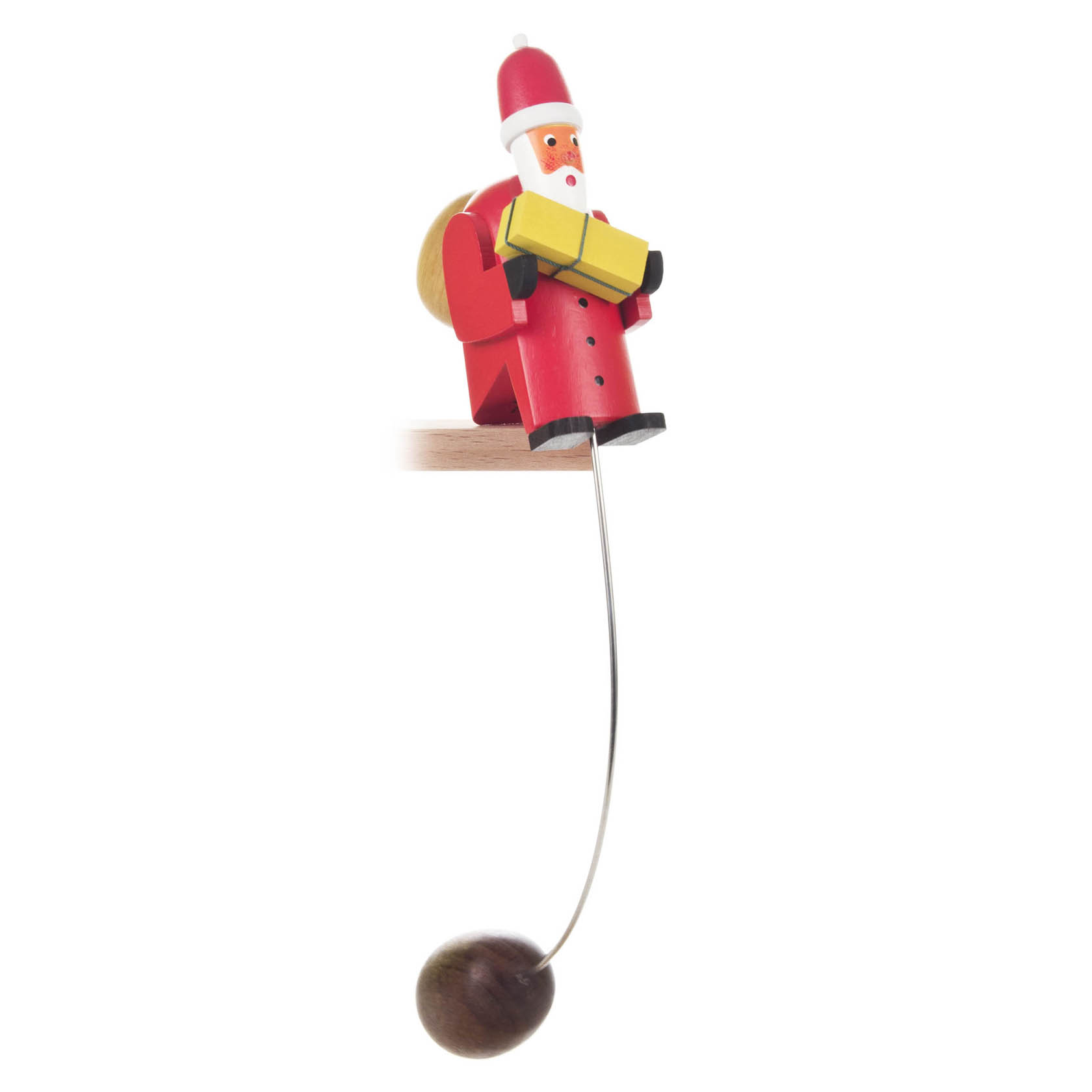 Kleine hölzerne Schaukelfigur eines Weihnachtsmanns, der ein gelbes Geschenk hält. Er sitzt auf einer Tischkante, unten hängt ein Gewicht an einem Draht. im Dregeno Online Shop günstig kaufen