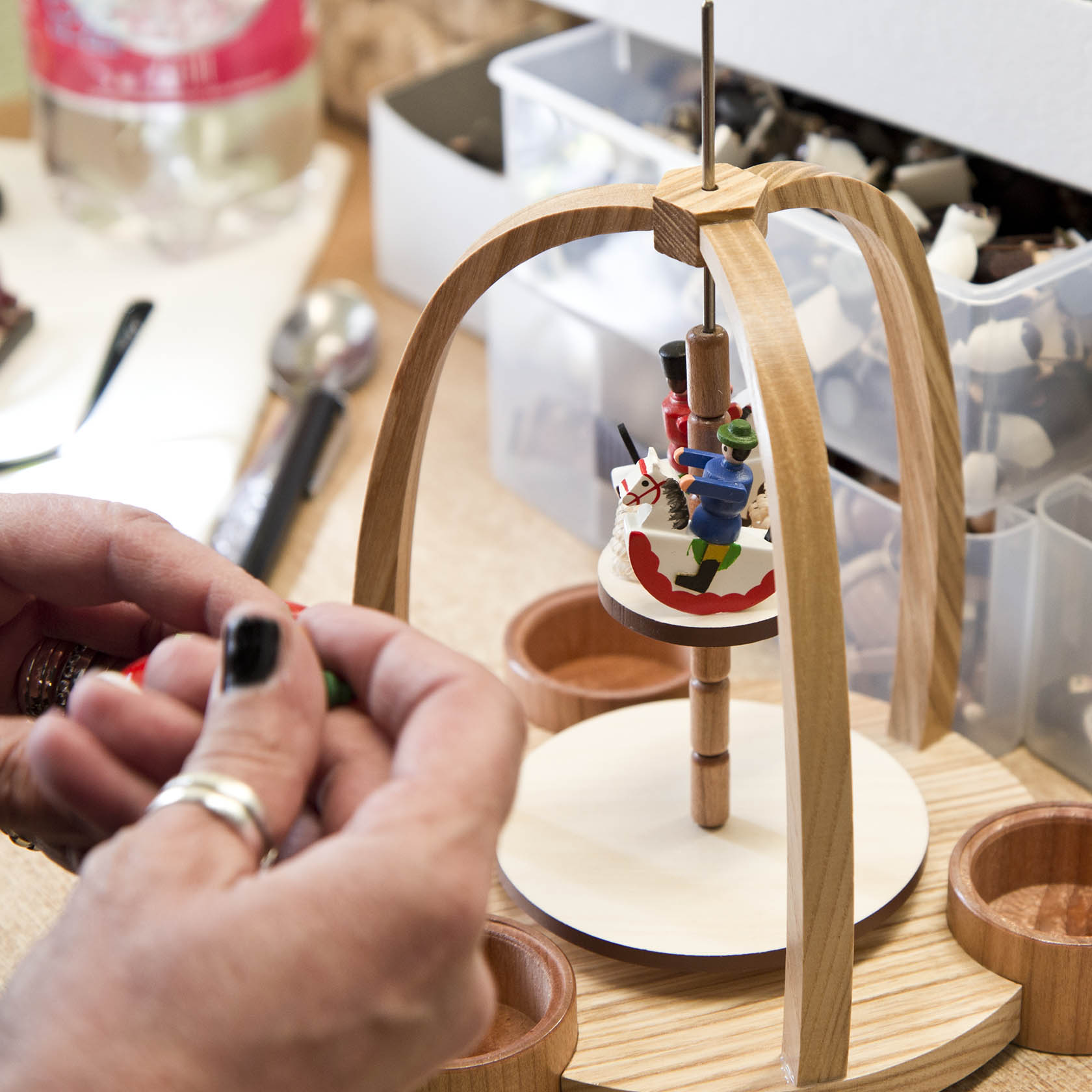 Zweistufige Weihnachtspyramide aus Holz in Bau. Oben ein Weihnachtsmann, unten Ring mit Reiterfiguren. Eine Person arbeitet an Details.