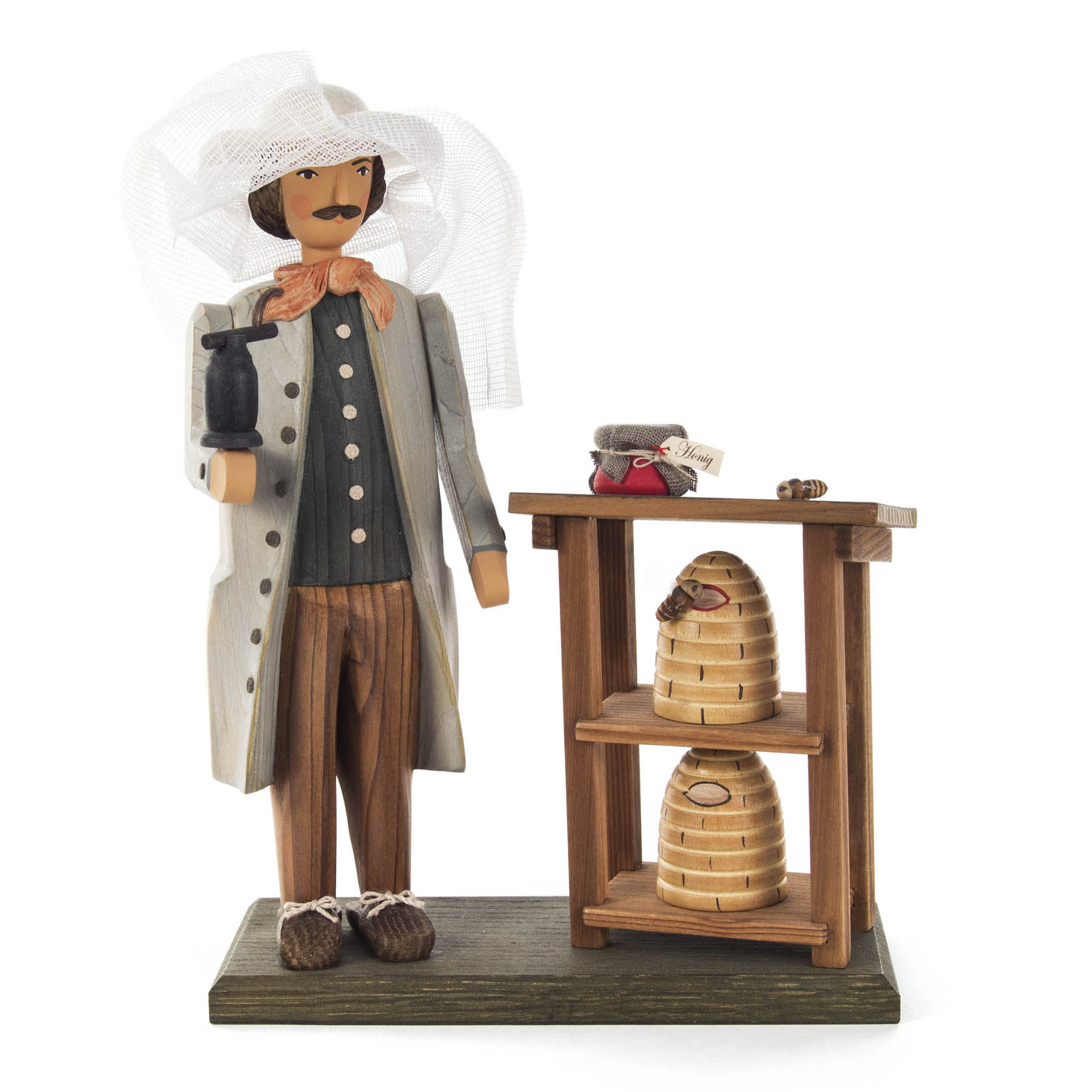 Holzfigur eines Imkers mit Schleier, der eine Pfeife hält, neben einem Tisch mit zwei Bienenkörben und weiteren kleinen Gegenständen. im Dregeno Online Shop günstig kaufen