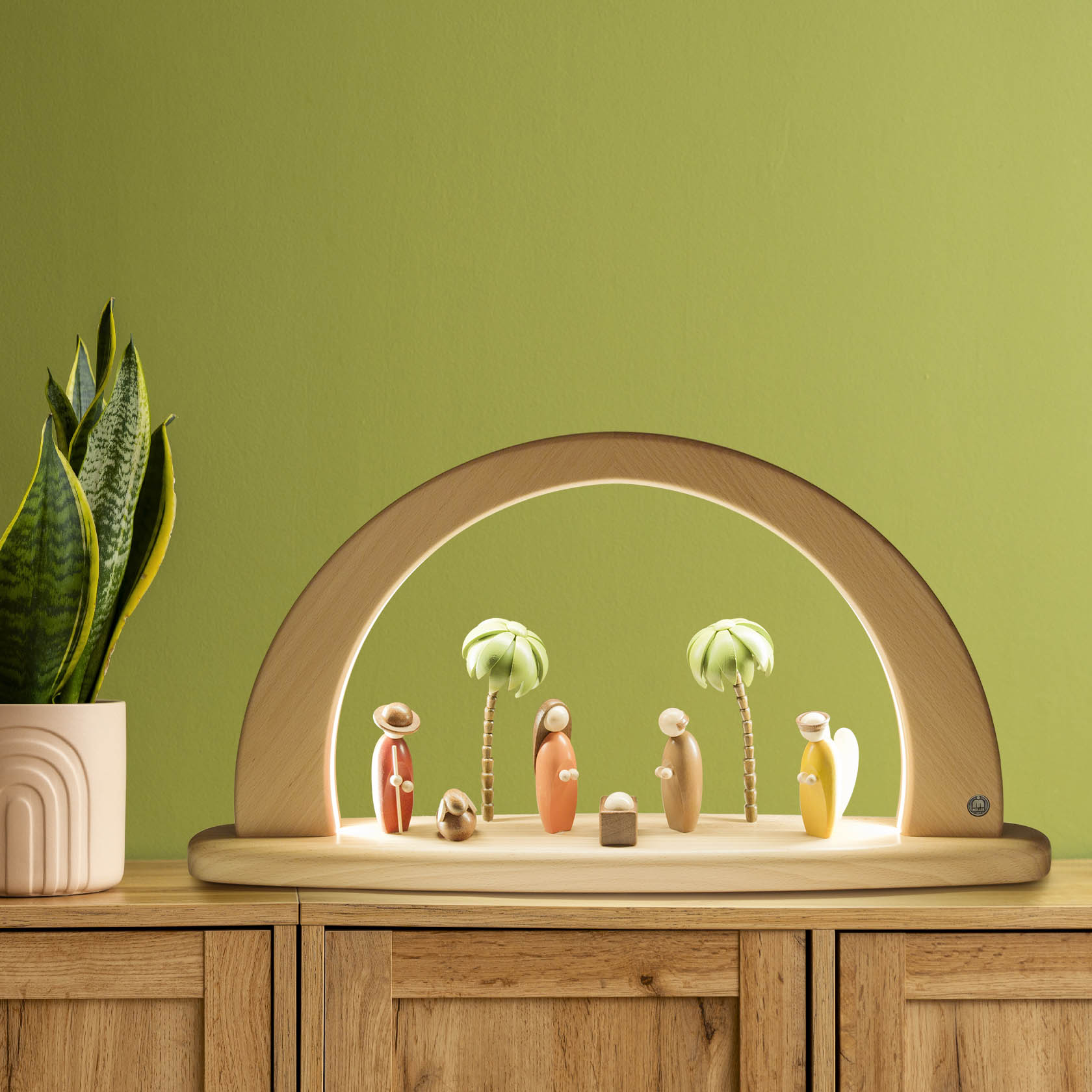 A wooden arch with LED lighting displaying a Nativity scene. There are colorful, minimalist figures of Mary, Joseph, Baby Jesus, and three palm trees.