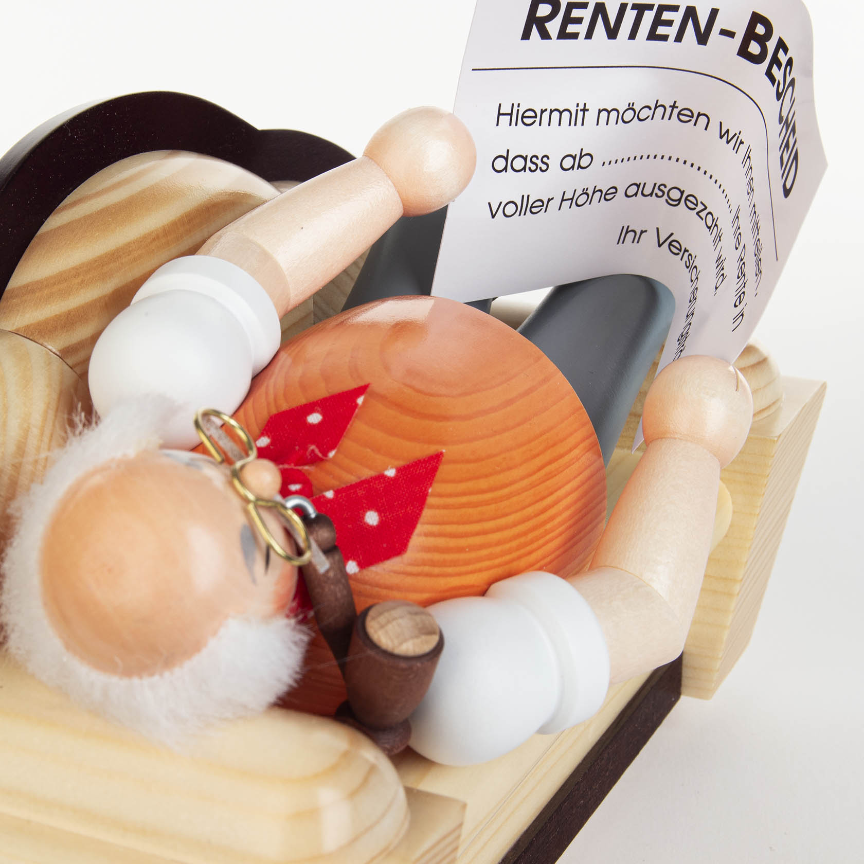 Wooden smoker figure of a retired man lying on a sofa, with a white beard, glasses, and a red scarf, holding a pipe and a retirement notice.