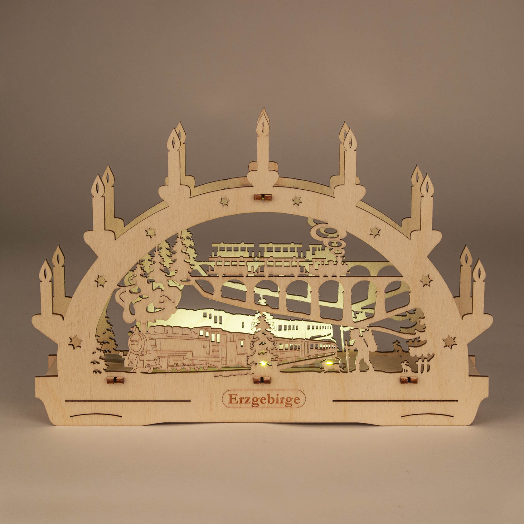 Ein Holzschwibbogen mit einem eingeschnittenen Motiv einer Eisenbahn, die über eine Brücke fährt, und LED-Beleuchtung. Aufschrift 'Erzgebirge'.