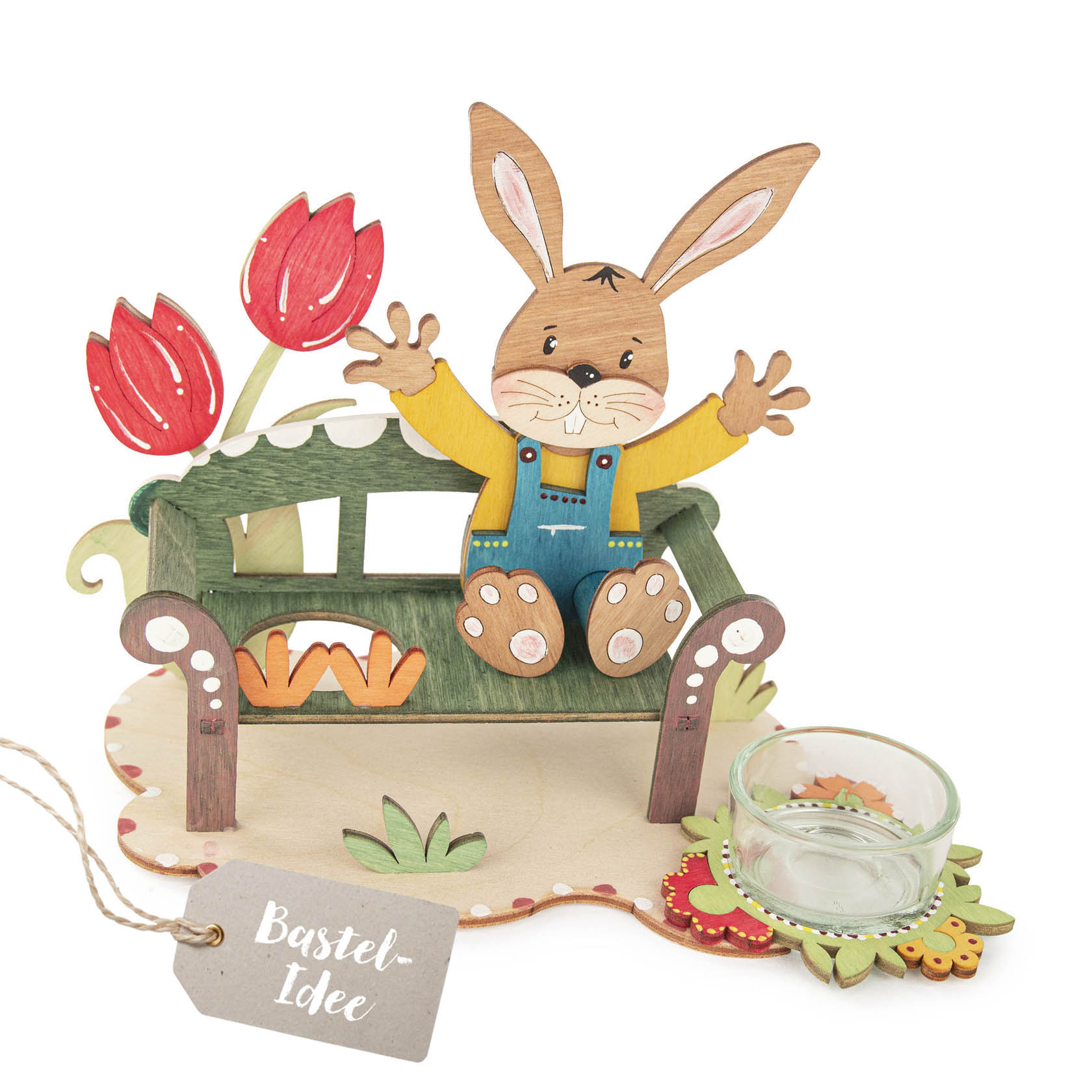 Bastelset mit einer grünen Bank und einem fröhlichen Hasen aus Holz. Der Hase sitzt auf der Bank. Daneben stehen rote Tulpen und ein Teelichtglas. im Dregeno Online Shop günstig kaufen