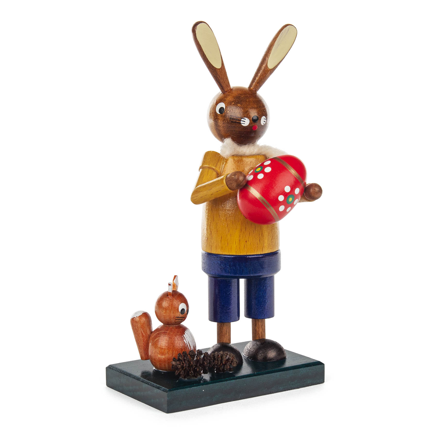 Eine stehende Holzfigur eines Osterhasen in gelbem Pullover und blauer Hose, der ein rotes Osterei hält. Daneben sitzt ein kleines Eichhörnchen und zwei Tannenzapfen liegen am Boden.