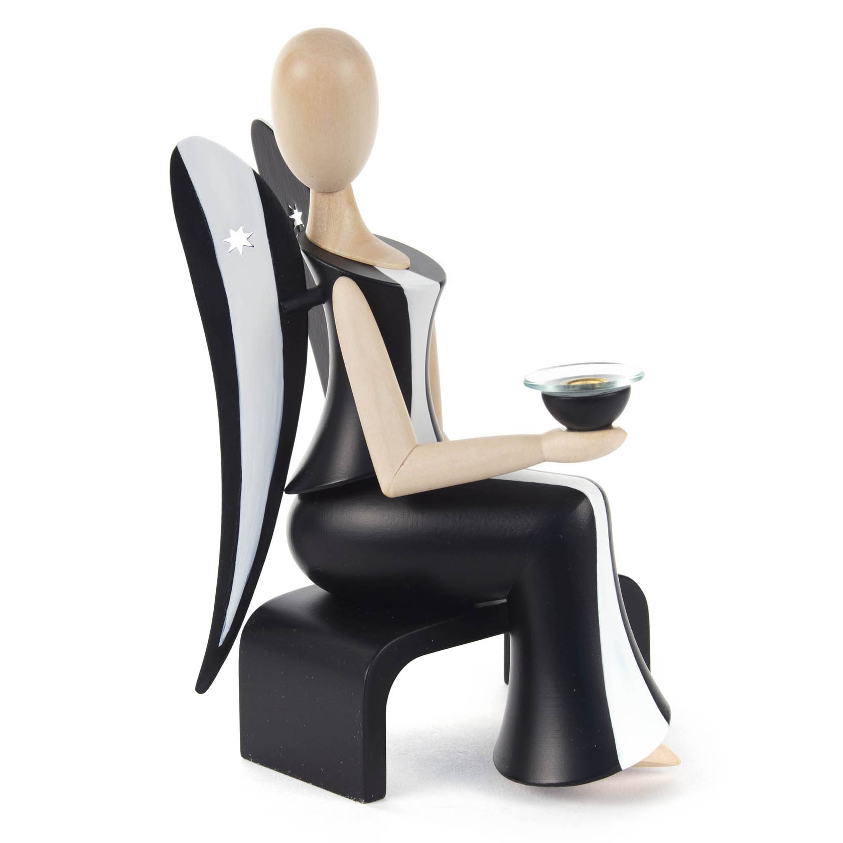 Holzengel in Schwarz-Weiß, sitzend, hält einen Kerzenhalter mit Glasschale. Flügel mit weißen Sternen. Figur ist 15,5cm hoch.