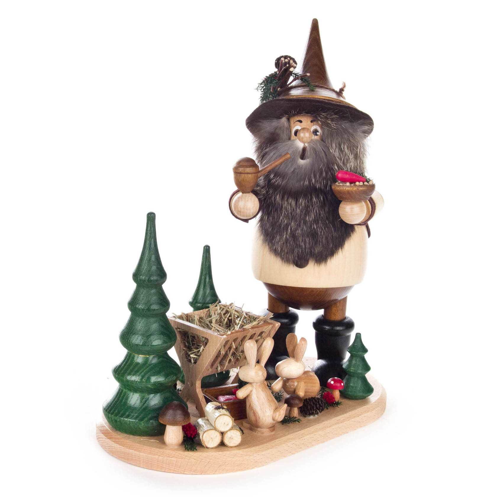Holzfigur eines Waldwichtels mit Pfeife und Bart, trägt Futterkrippe mit Karotten. Umgeben von zwei grünen Bäumen, Hasenfiguren und Pilzen auf Holzplatte. im Dregeno Online Shop günstig kaufen