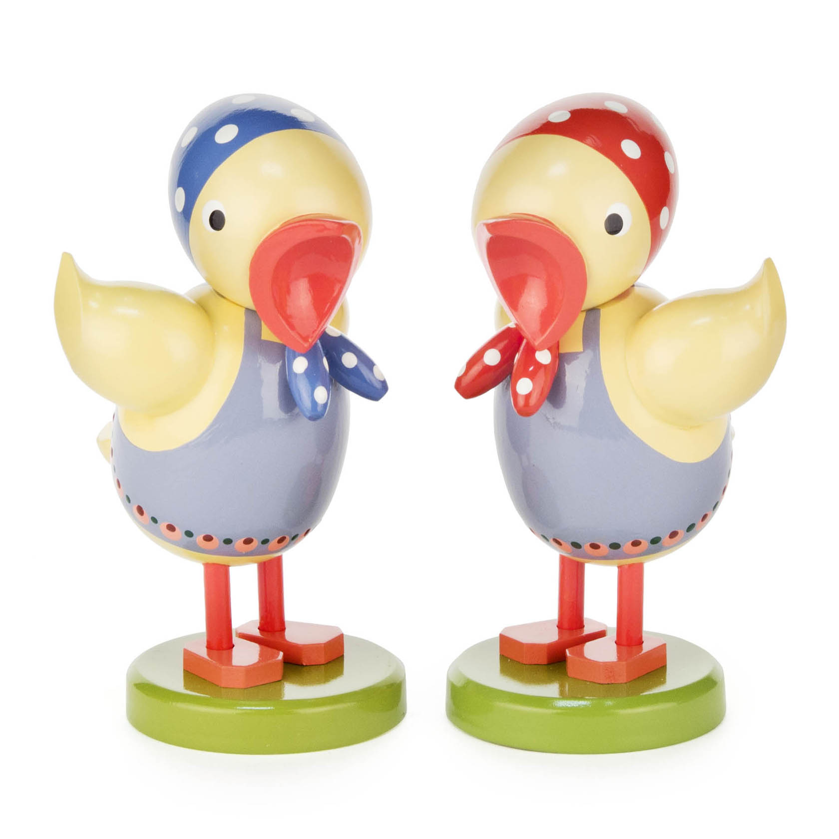 Zwei Holzfiguren in Form von Küken mit roten und blauen Kopftüchern, die auf grünen Sockeln stehen. im Dregeno Online Shop günstig kaufen