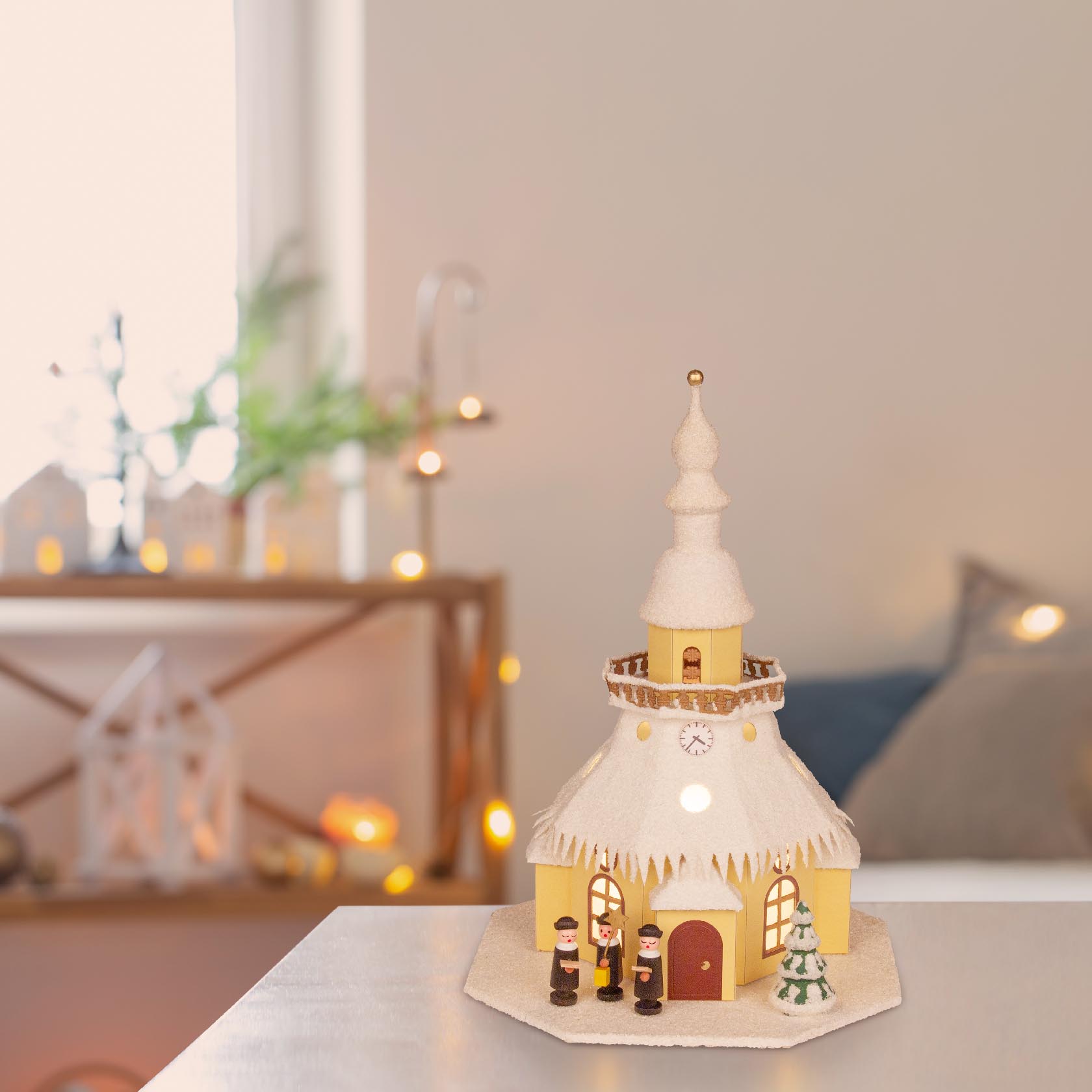 Kleines Lichterhaus in Form der Seiffener Kirche mit elektrischer Beleuchtung. Vor der Kirche stehen drei kleine Holzfiguren und ein Tannenbaum.