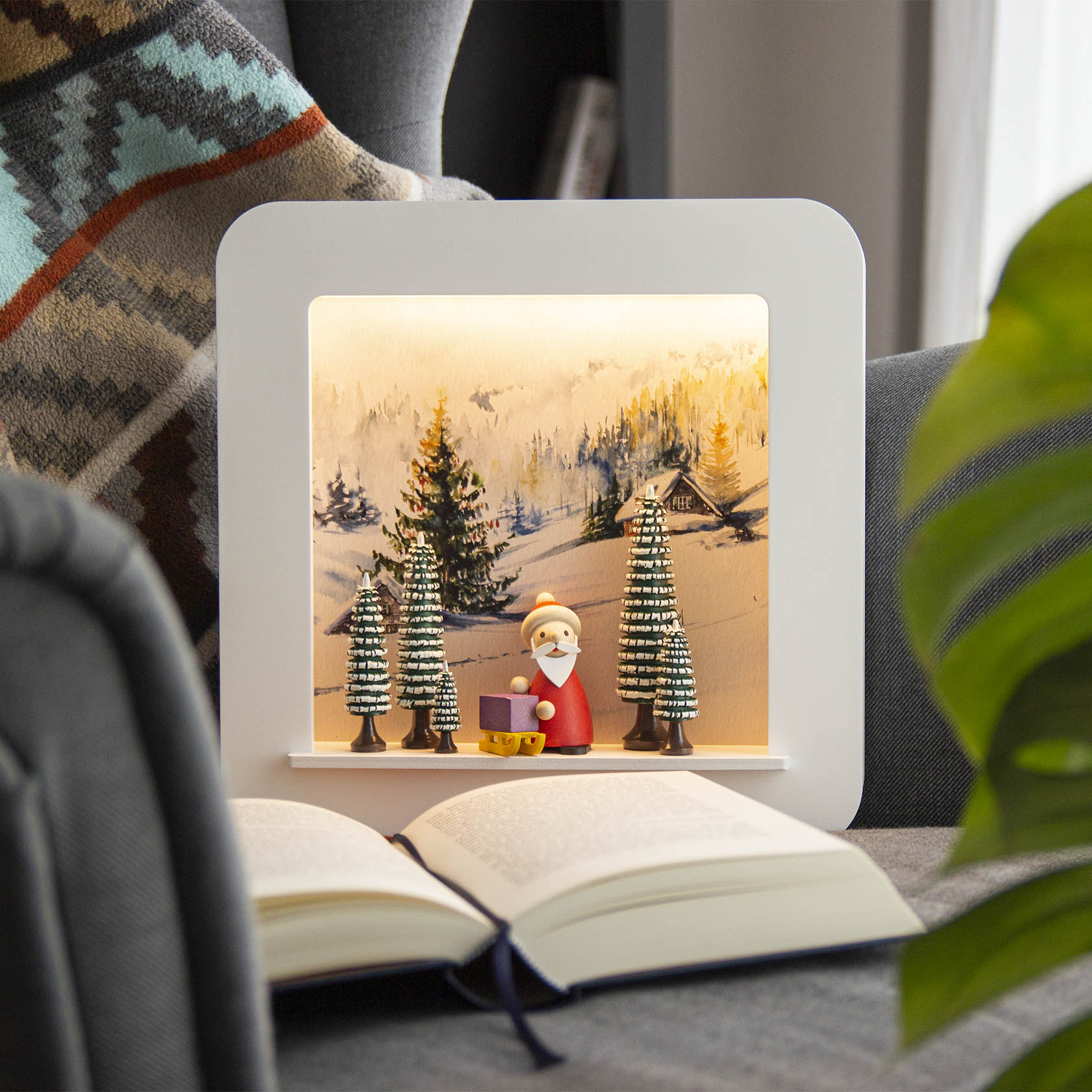 Dekoratives Lichtrahmenbild eines Winterwaldes mit fünf grün-weiß geringelten Bäumen und einer Weihnachtsmannfigur, die einen lila Schlitten zieht.