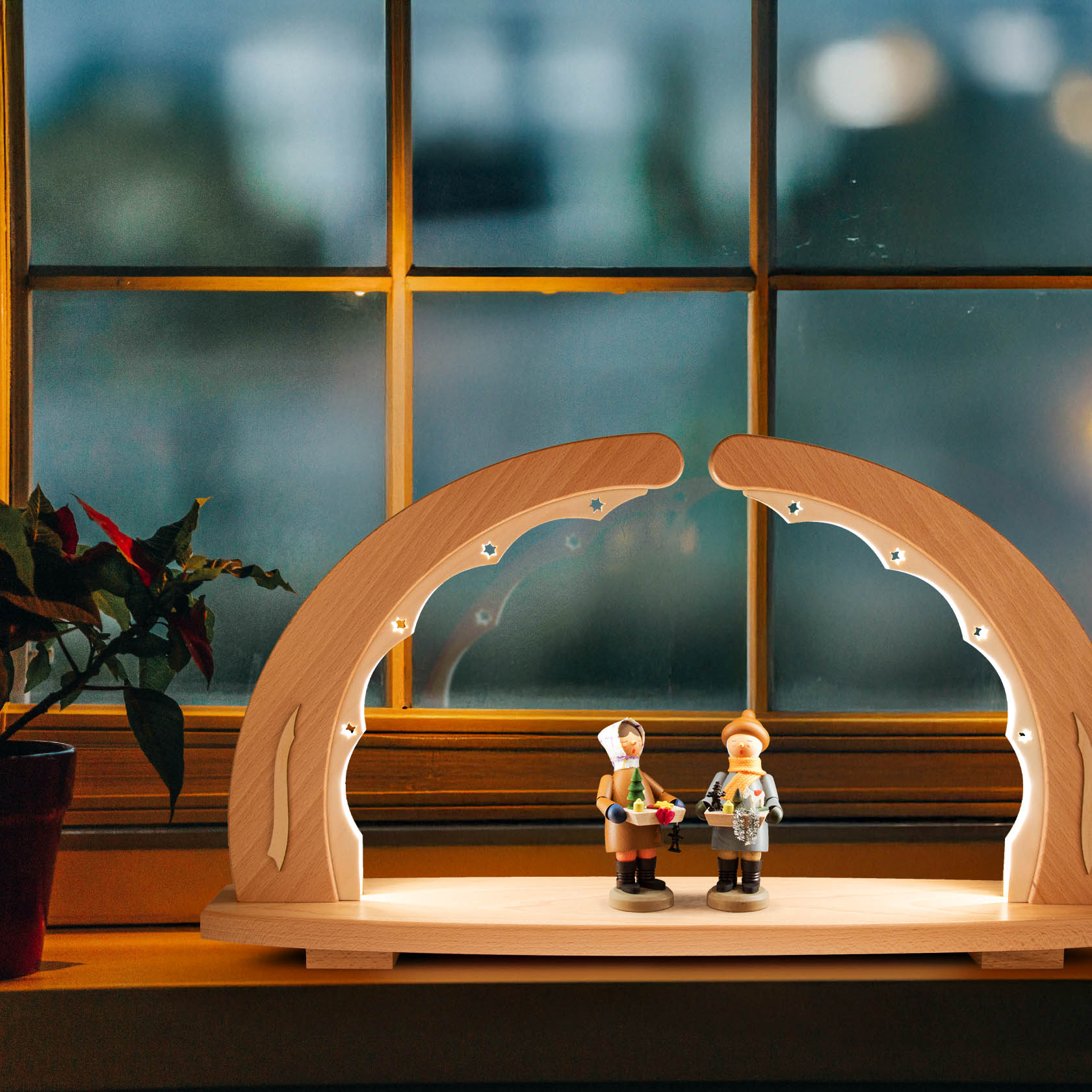 Ein Schwibbogen aus Holz, unbestückt und indirekt mit LEDs beleuchtet. Im Vordergrund sind zwei Figuren auf der Basis des Bogens platziert.