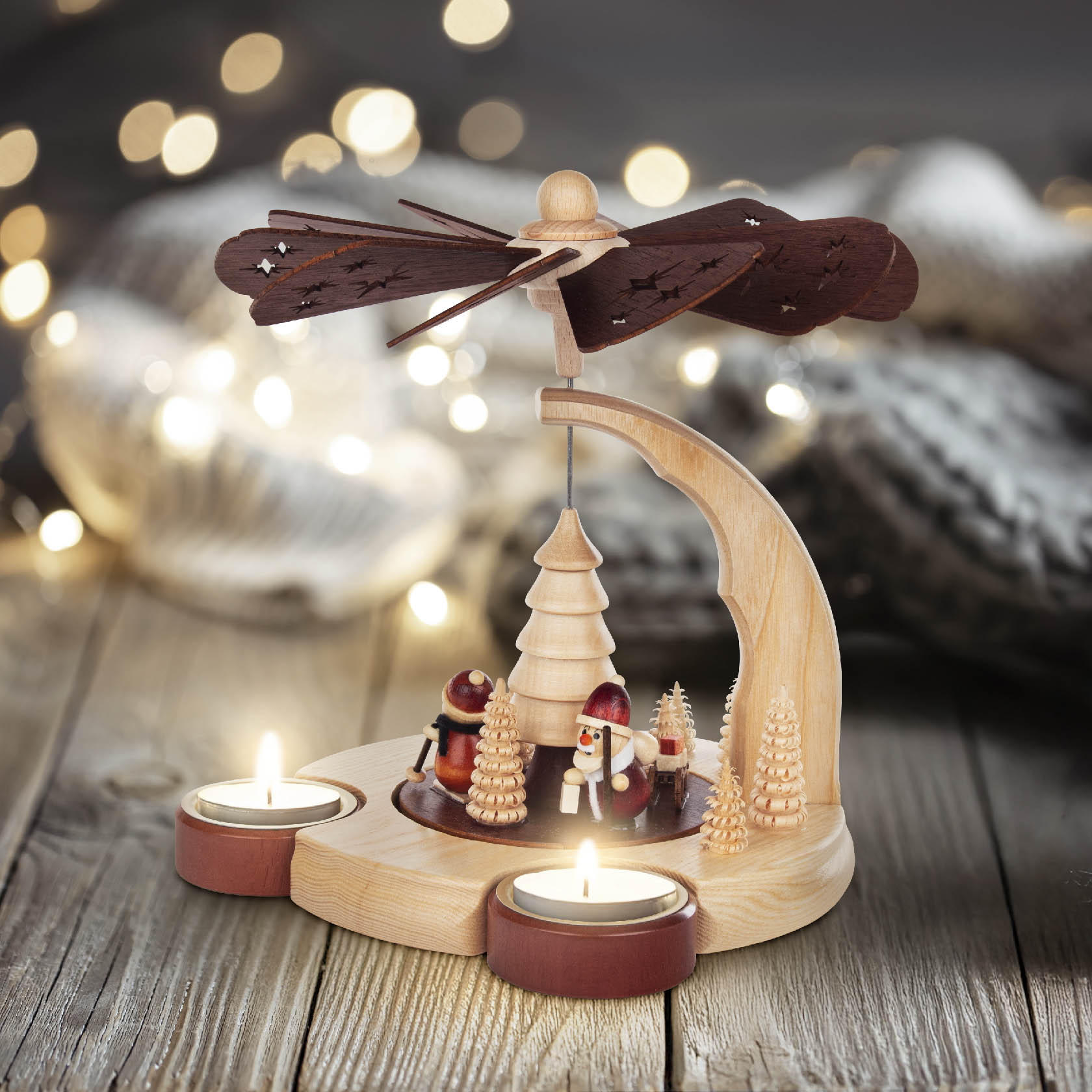 Weihnachtspyramide aus Holz mit Teelichthaltern, kleinen Holzfiguren von Weihnachtsmännern und einem Baum, angetrieben durch ein Windrad.
