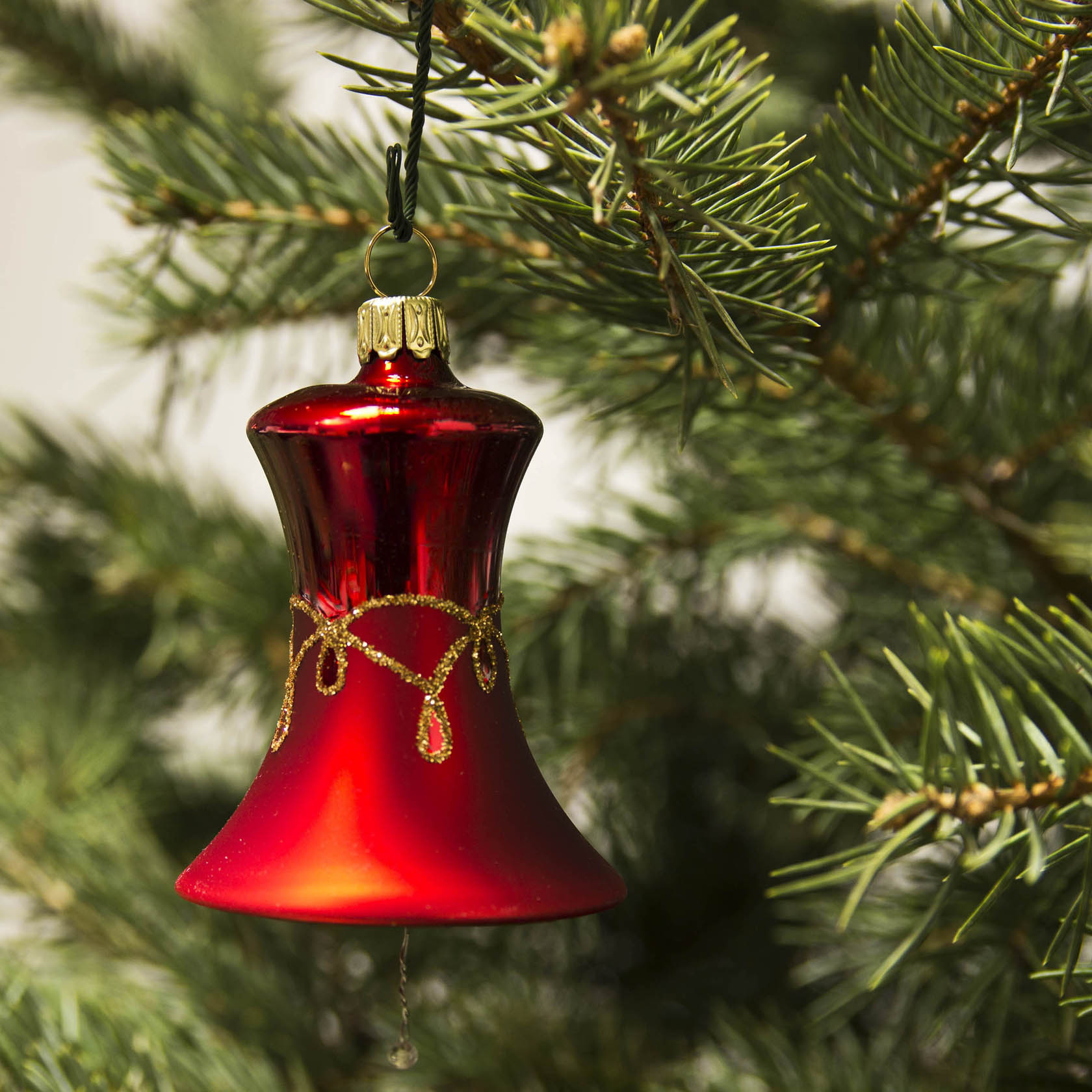 Red-matte bell-shaped Christmas ornament with drop pattern hanging on a Christmas tree branch.