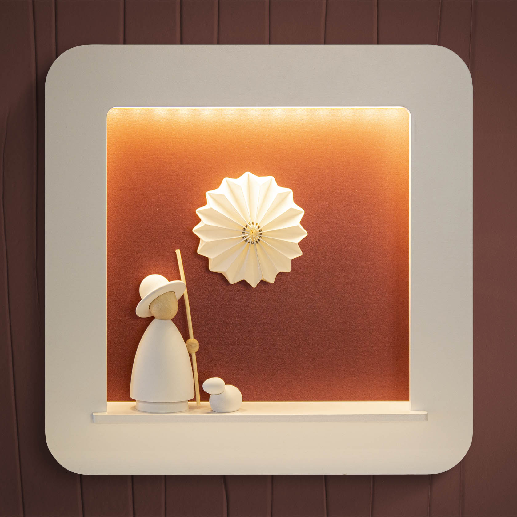 Minimalistische Holzfigur eines Schäfers mit Hut und Stab neben einem weißen Schaf, vor einem orange-braunen Hintergrund mit dekorativer Blumenform.