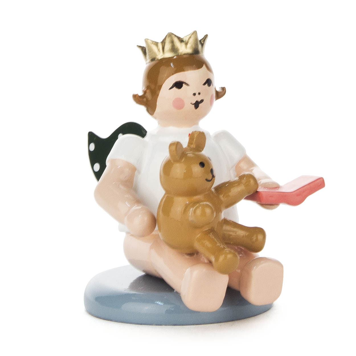 A seated angel figure with a golden crown, holding a teddy bear and a red book. The angel has wings and is wearing a white outfit. im Dregeno Online Shop günstig kaufen