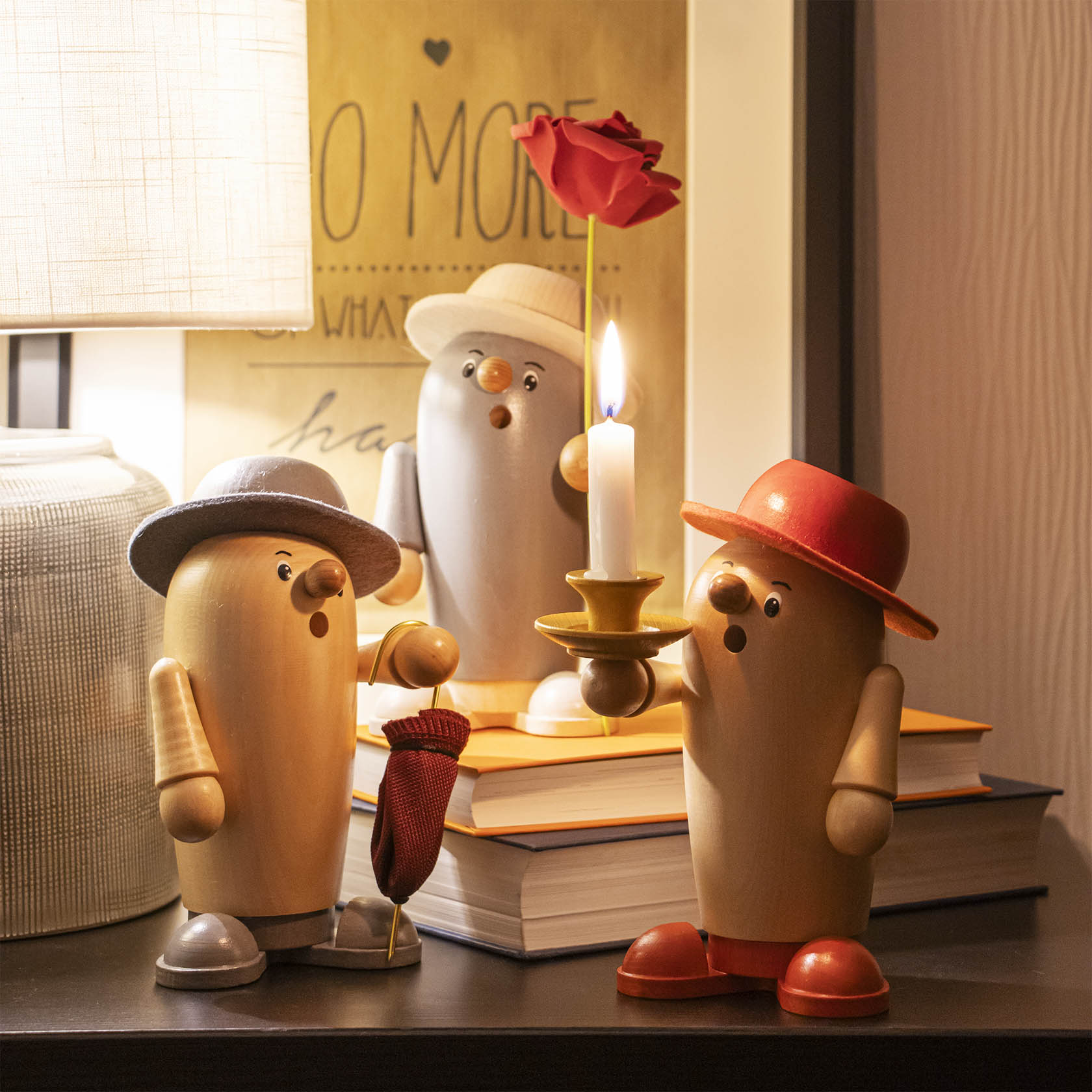 Drei Holzräucherfiguren in Form von Pinguinen. Der vordere trägt einen roten Hut, hält eine Rose und einen Kerzenhalter. Die anderen tragen graue Hüte.