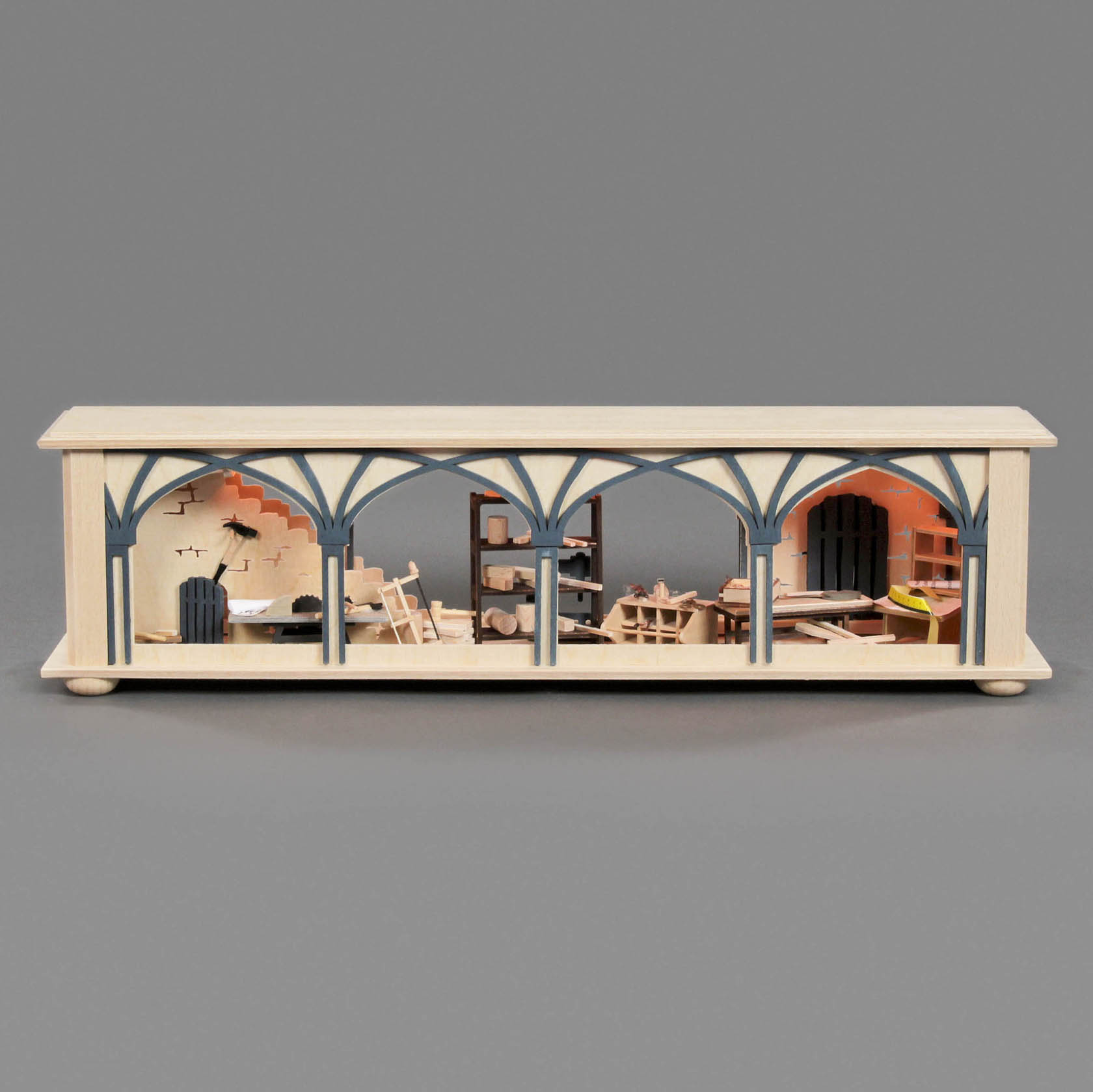 Ein kleiner, elektrisch beleuchteter Miniatur-Universalsockel mit einer Holzwerkstatt-Darstellung, inklusive Werkbänke, Werkzeug und Regale.
