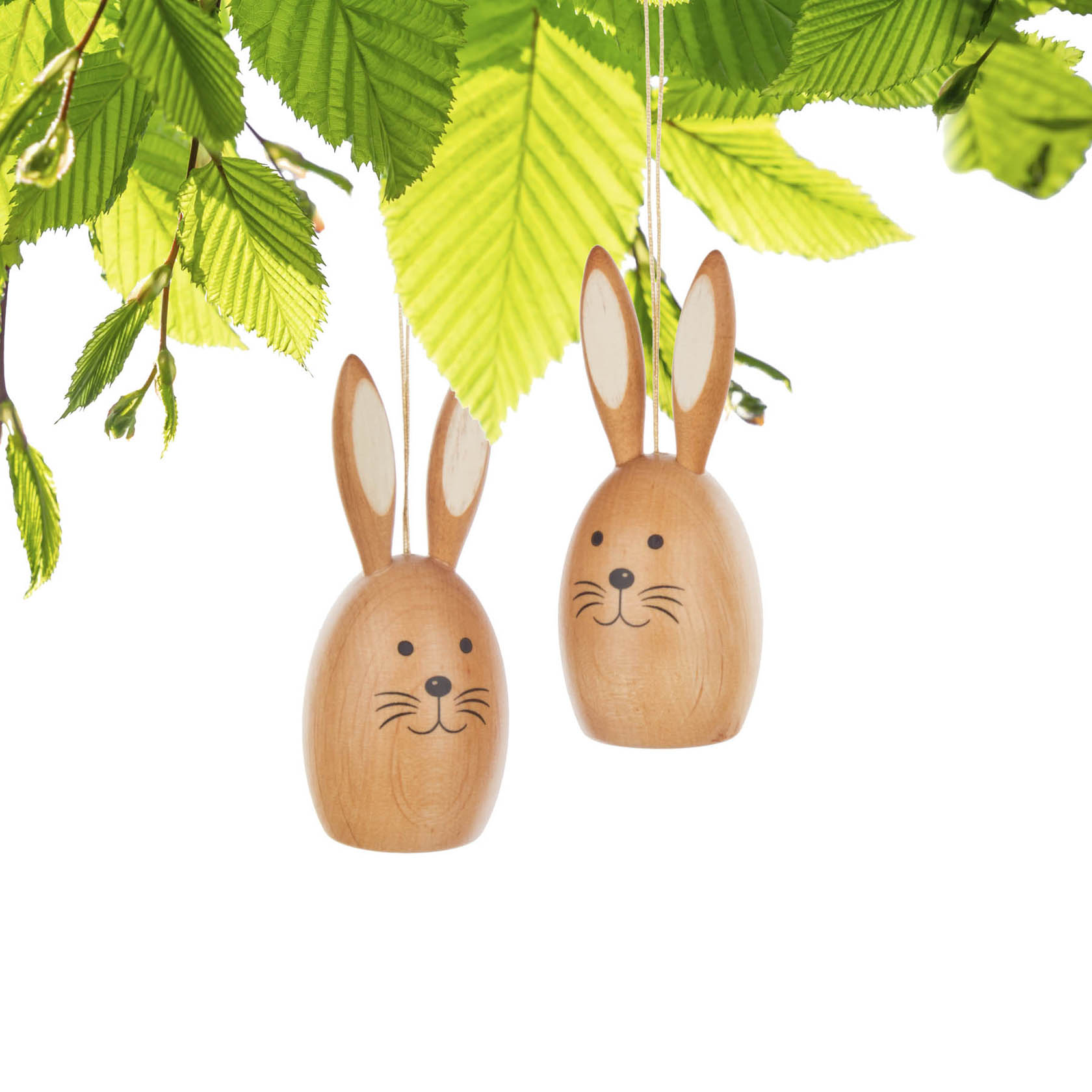 Zwei hölzerne Hasenfiguren mit langen Ohren und gemalten Gesichtern, die an einer Schnur hängen, vor grünen Blättern.