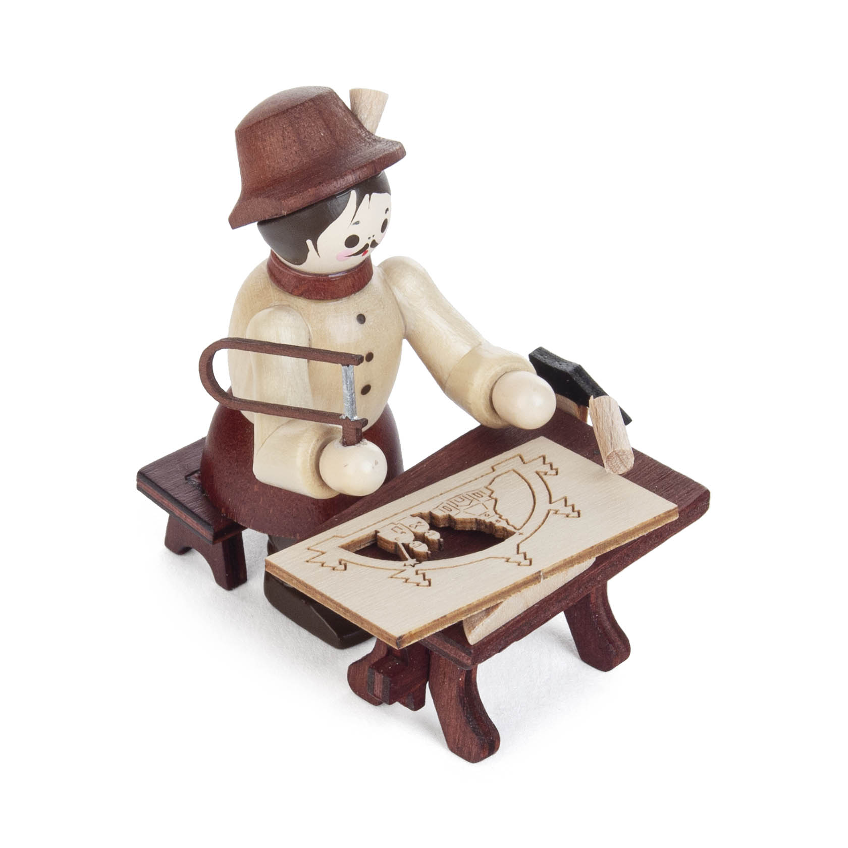 Holzfigur eines Handwerkers mit Hut und Schürze. Er sitzt an einem Tisch, sägt an einem hölzernen Schwibbogenmotiv und hält einen kleinen Hammer.