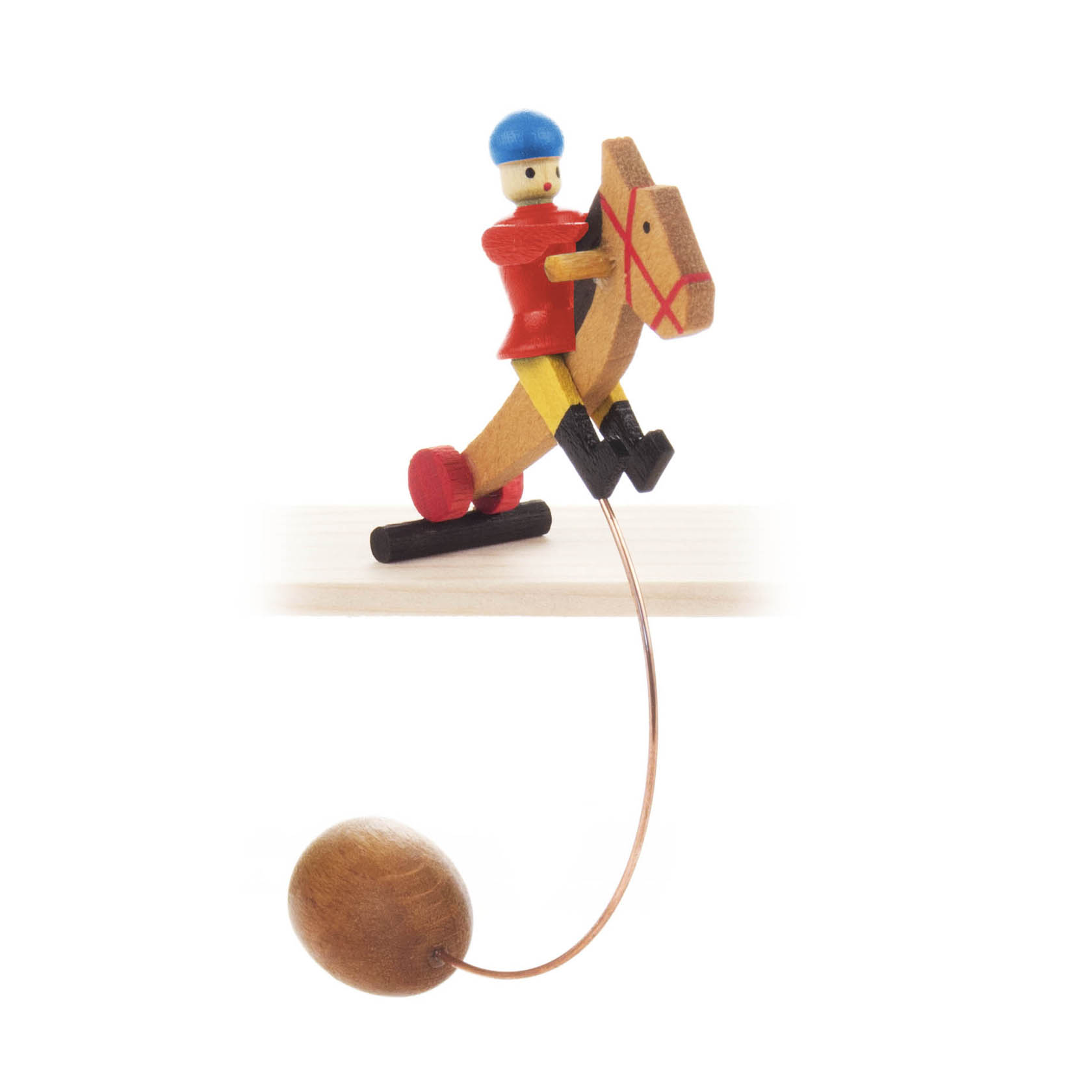 Kinderspielzeug aus Holz: Ein Reiter in Rot mit blauem Helm auf einem Pferd auf einer Wippe. Der Wippmechanismus wird durch eine Kugel an einem Draht betätigt. im Dregeno Online Shop günstig kaufen