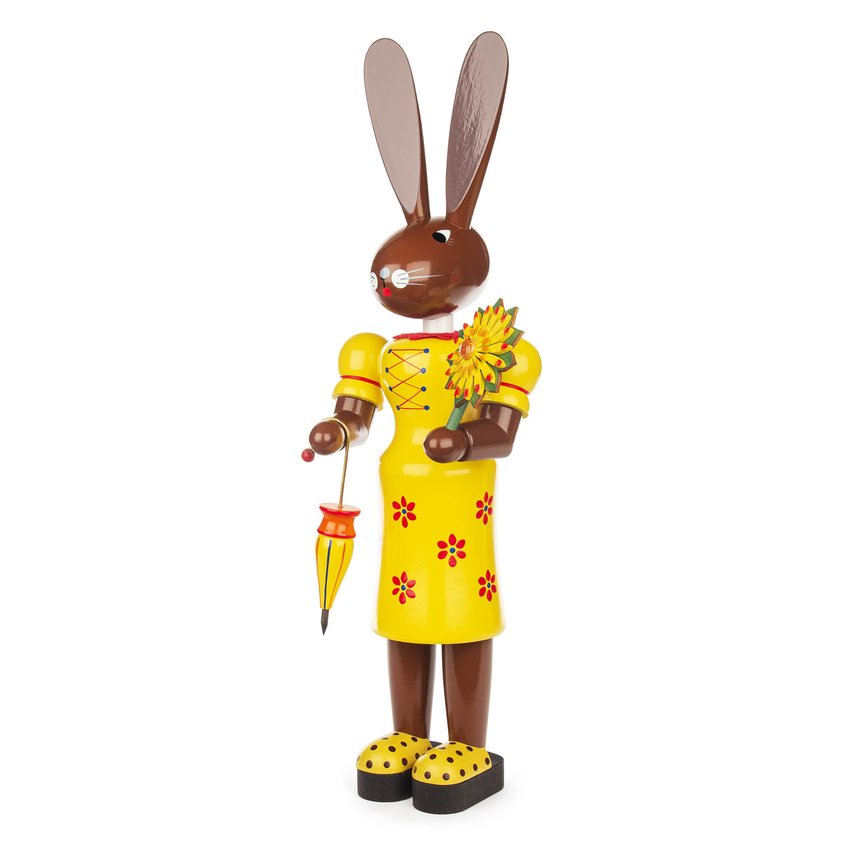 A wooden bunny figure in a yellow dress with red flowers, holding an umbrella and a sunflower.