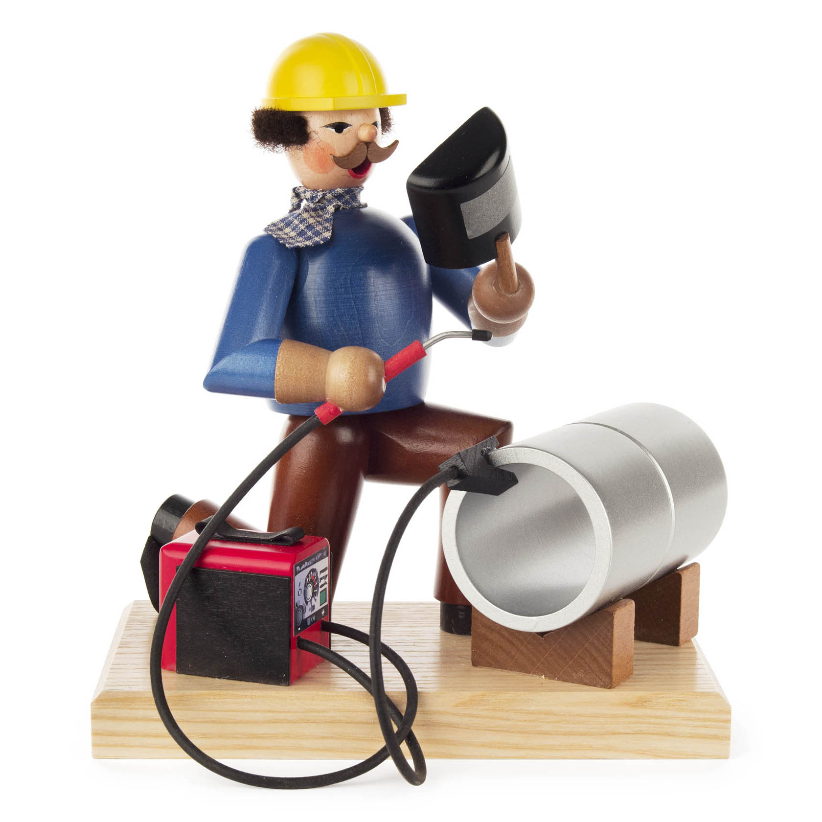 Holzfigur eines Schweißers mit gelbem Helm, der eine Pfeife hält und vor einem geschweißten Rohr kniet, samt Schweißgerät. im Dregeno Online Shop günstig kaufen