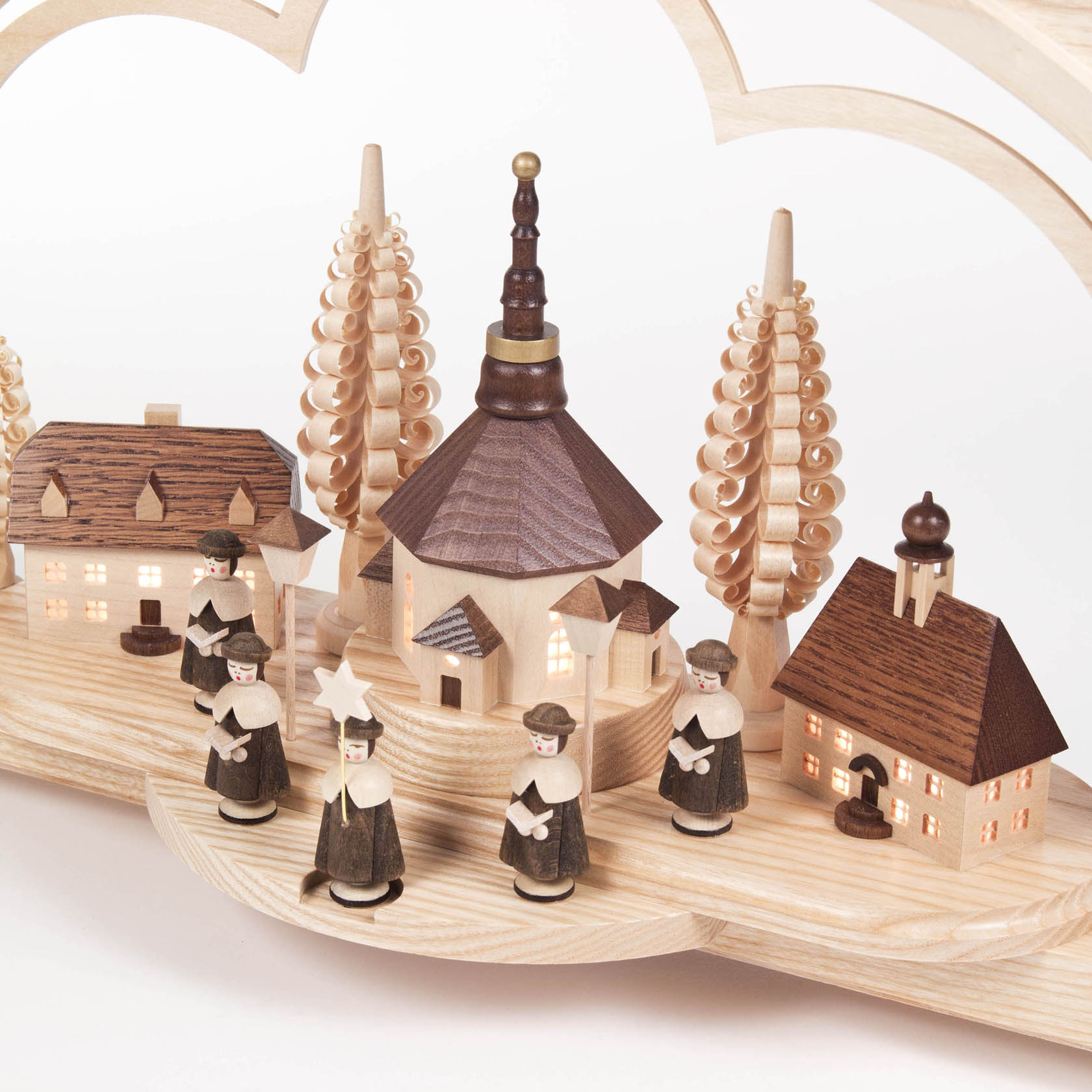 Ein Schwibbogen aus Holz zeigt ein Seiffener Dorf mit Kurrendesängern. Die Häuser und Kirche sind von innen beleuchtet, umrahmt von kunstvollen Bäumen.
