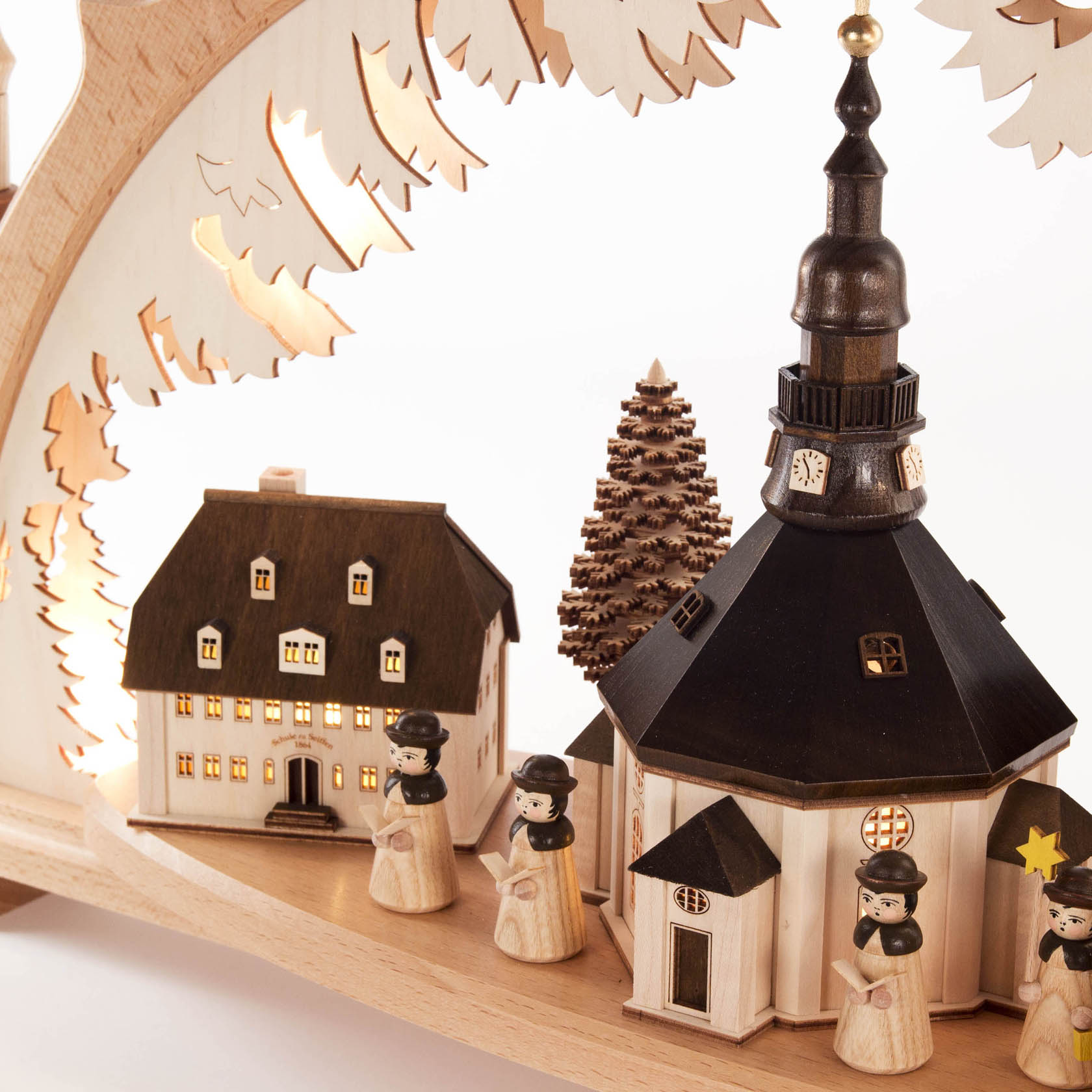 Holzschwibbogen mit beleuchteten Gebäuden und Kurrendefiguren, die eine Kirche und ein Haus flankieren. Die Kirche hat einen hohen Turm, Details durchleuchtet.