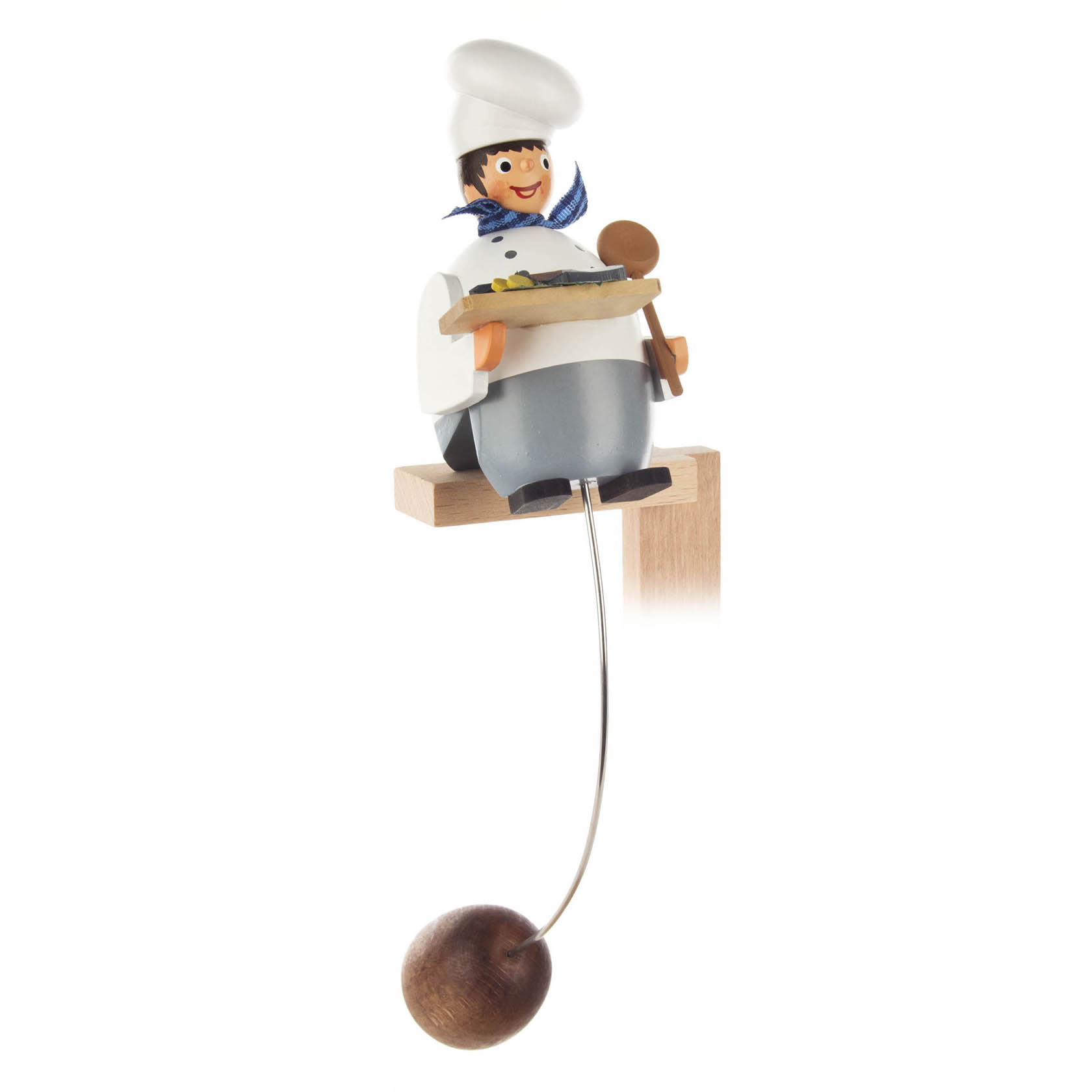 Holzschaukelfigur eines lächelnden Kochs mit Kochmütze, blauem Halstuch und einem Löffel in der Hand, auf einem Holzbalken sitzend. Eine Kugel hängt an einem Draht darunter. im Dregeno Online Shop günstig kaufen