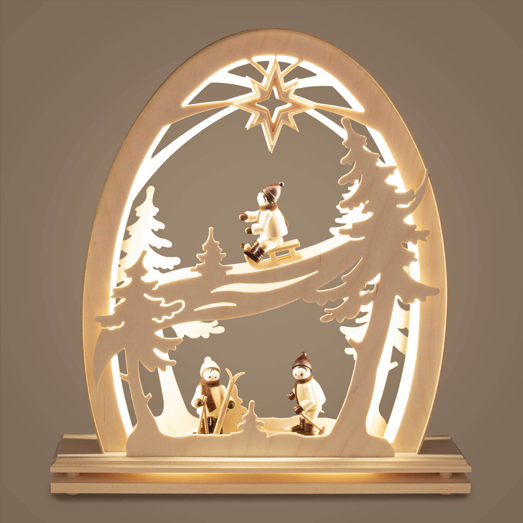 Beleuchteter Erzgebirgsbogen aus Holz mit Wintersportler-Motiven. Kinder mit Schlitten und Skiern, umgeben von Tannen und einem leuchtenden Stern.
