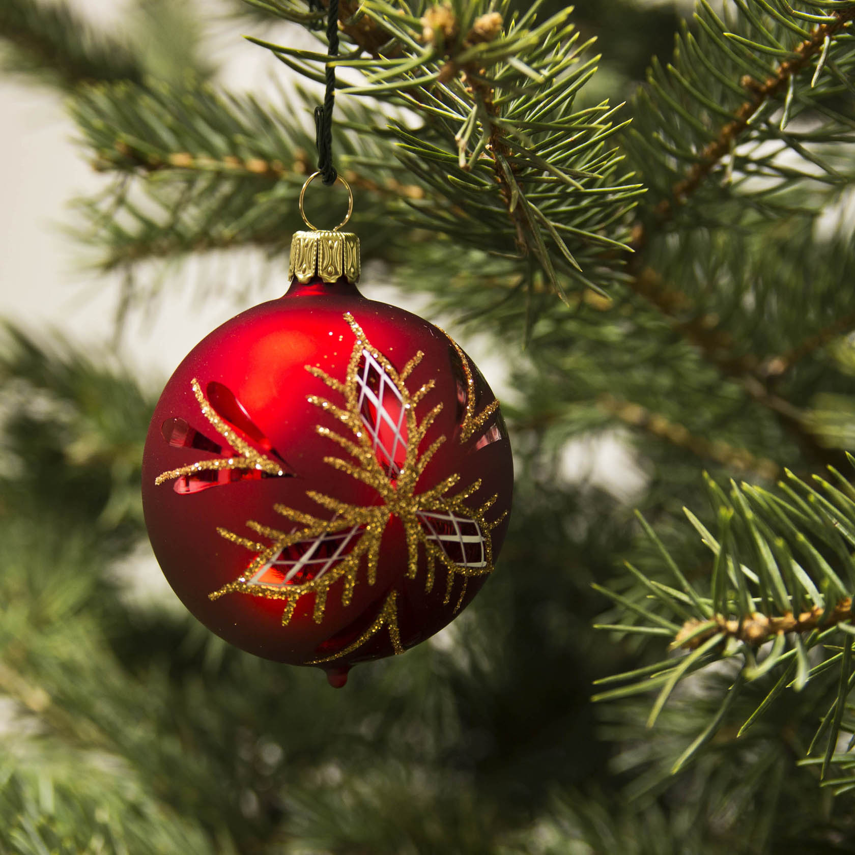 Eine rote Weihnachtskugel mit mattem Finish und einem goldenen Waffelmuster hängt an einem Tannenbaum.