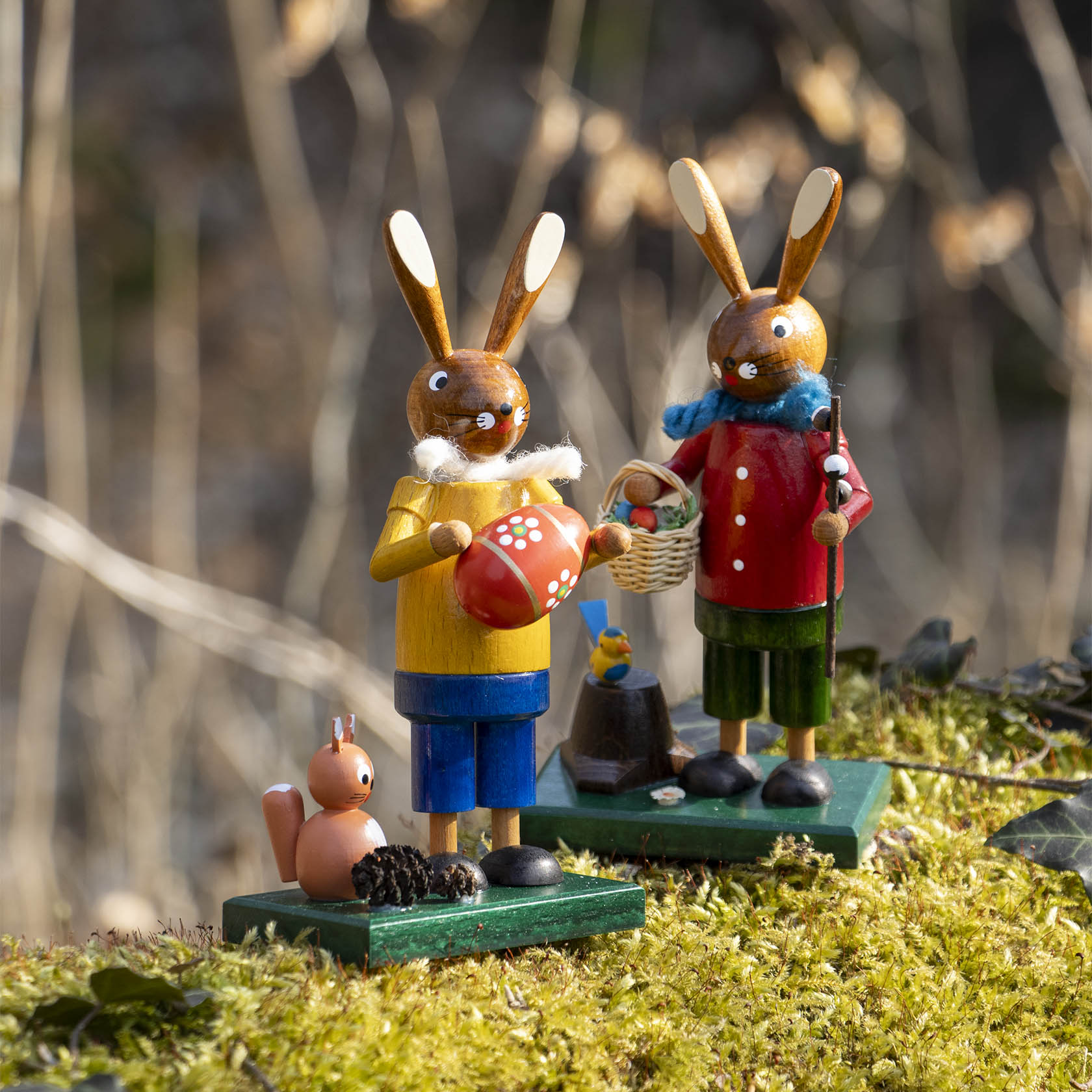 Zwei hölzerne Osterhasenfiguren, links ein gelber Hase mit rotem Herz, daneben ein kleines Eichhörnchen.