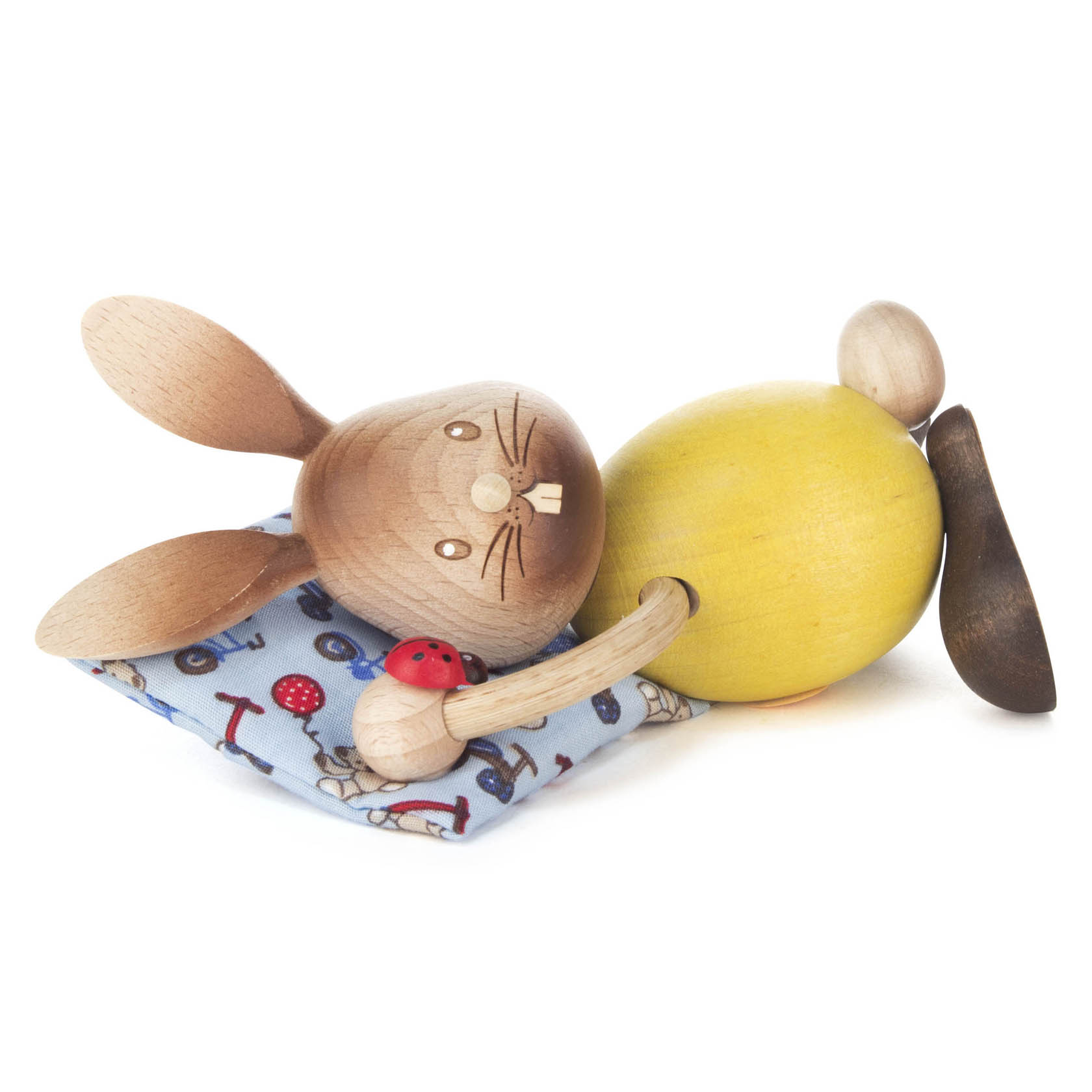Holzhase mit gelbem Körper und braunen Ohren liegt auf einem blauen Kissen mit Pilzmotiv, hält einen roten Marienkäfer aus Holz. im Dregeno Online Shop günstig kaufen