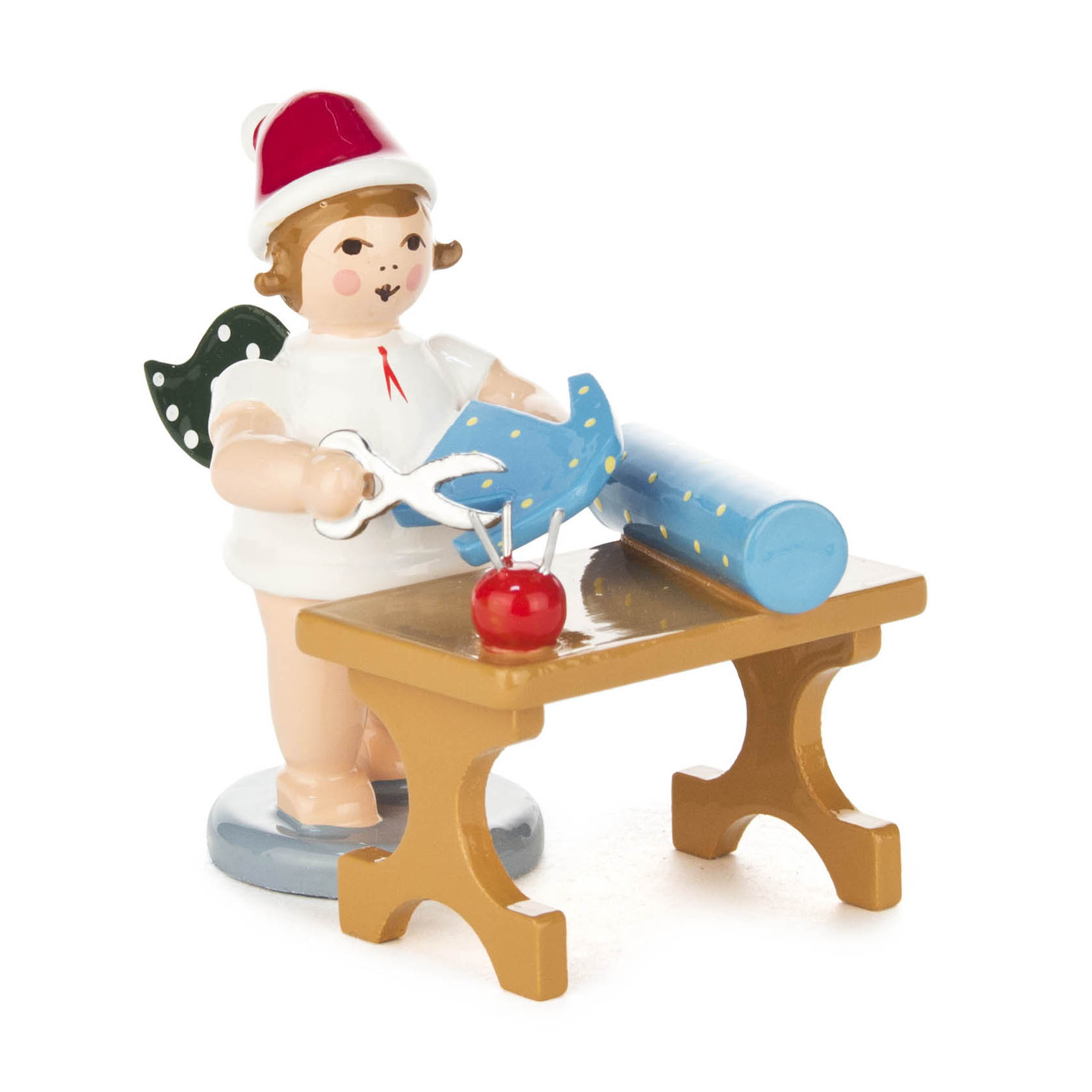 A small angel figurine in white with wings, wearing a red hat, holding scissors and cutting blue fabric on a tailor's table. im Dregeno Online Shop günstig kaufen