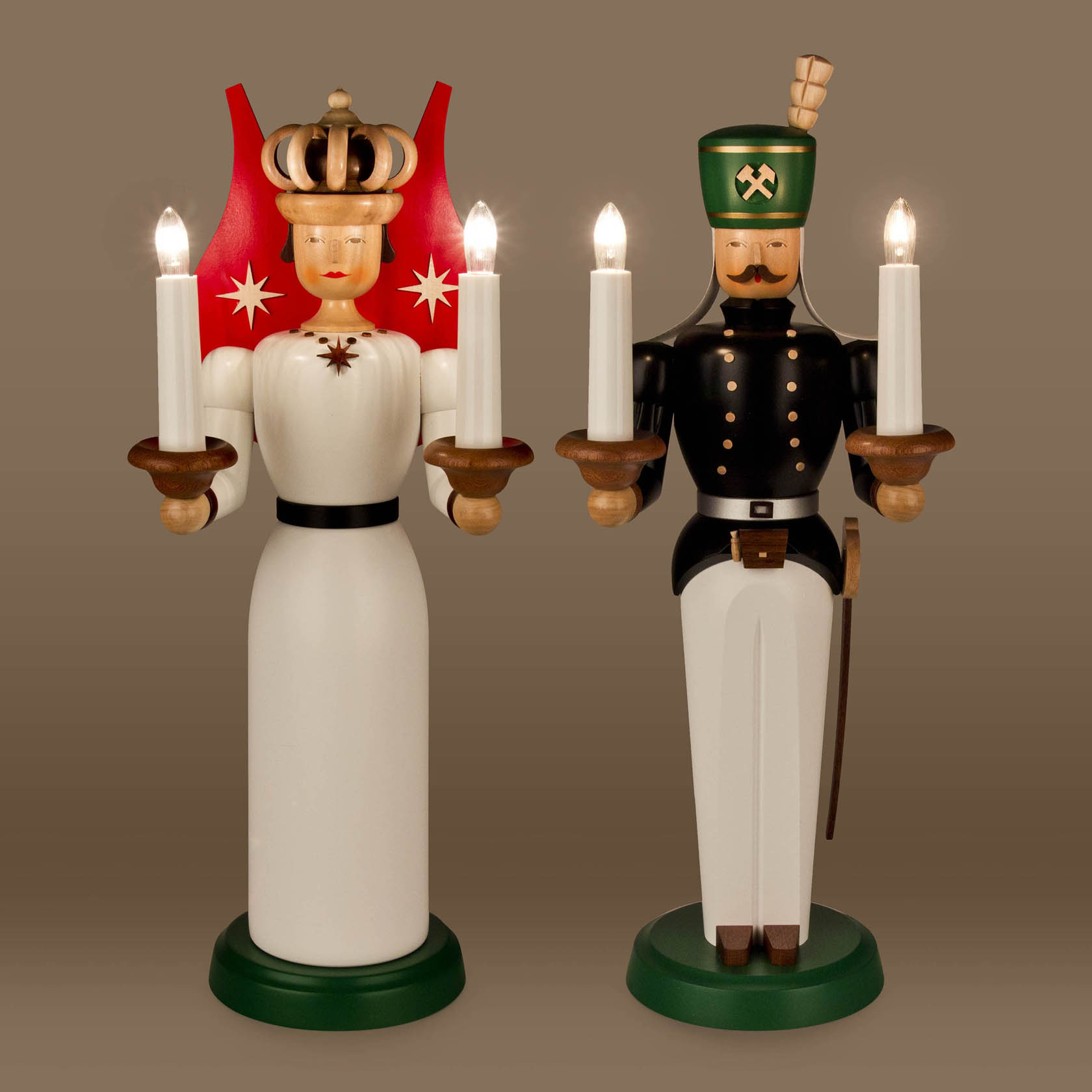 Zwei traditionelle Holzfiguren, ein Engel in weißem Kleid mit Krone und ein Bergmann in Uniform, beide halten leuchtende Kerzen in den Händen.