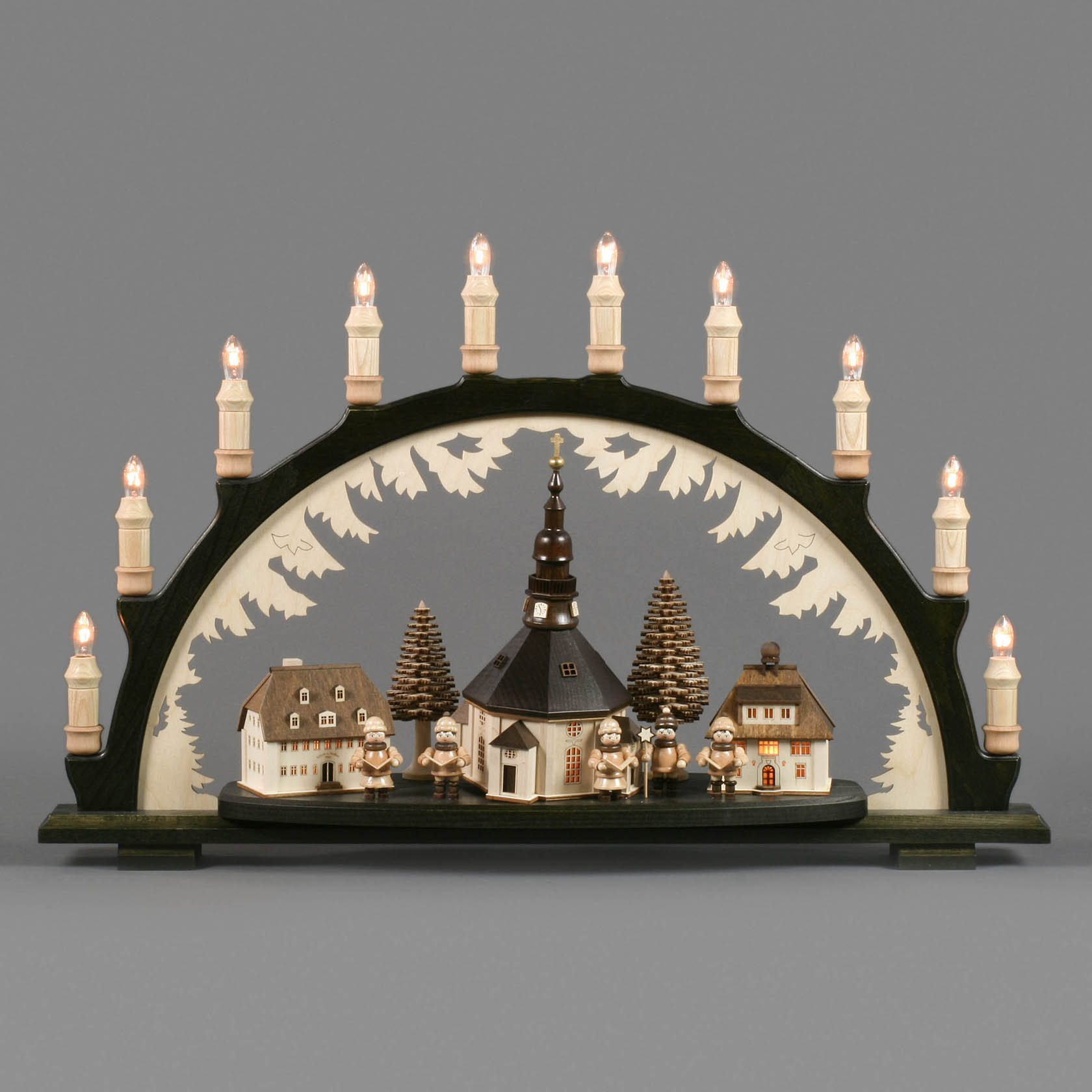 Ein schwarzer Schwibbogen mit einem Seiffener Dorf, das eine Kirche und Kurrende-Sänger zeigt, umgeben von innenbeleuchteten Gebäuden und LED-Kerzen.