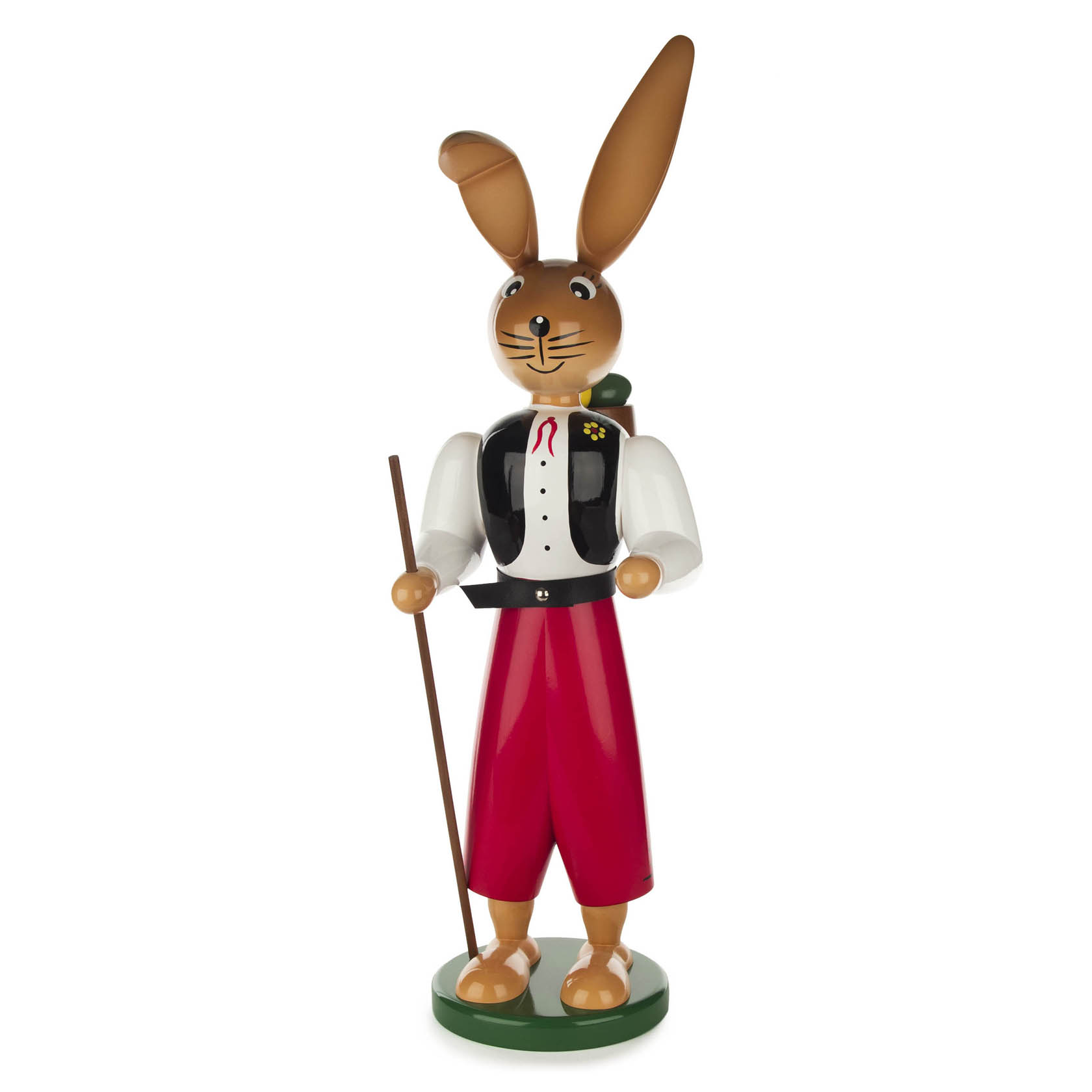 Holzfigur eines stehenden Hasen mit braunem Fell und langen Ohren, einem Wanderstock, trägt rote Hose, schwarze Weste, weißes Hemd und Fliege.