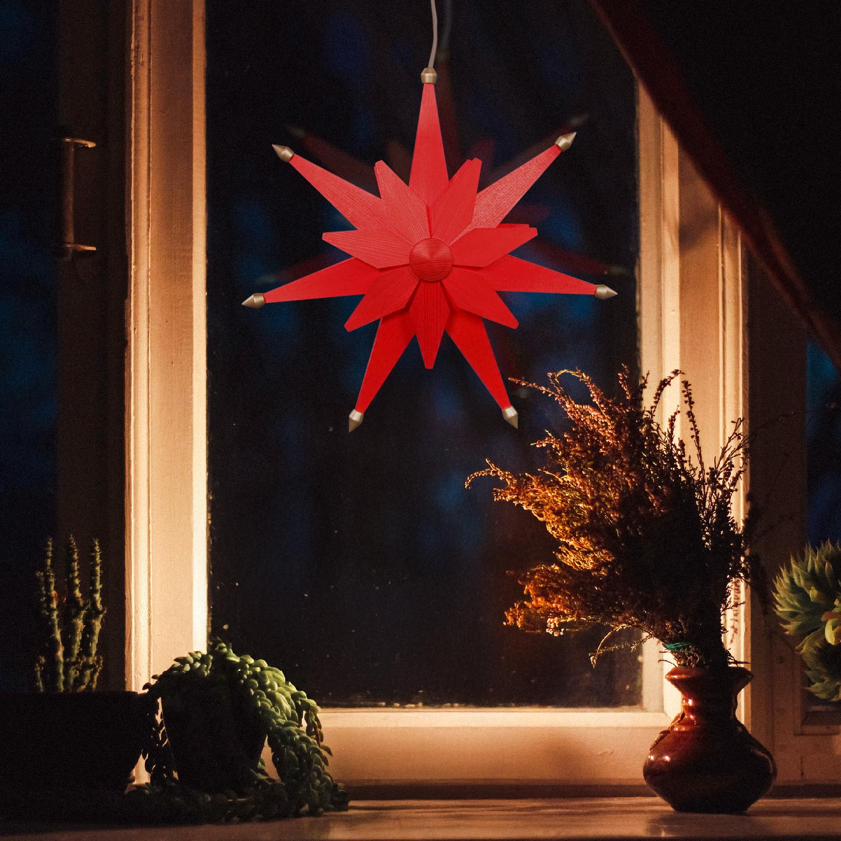 Roter doppelschichtiger Weihnachtsstern mit elektrischer Beleuchtung, aufgehängt an einem Fenster.