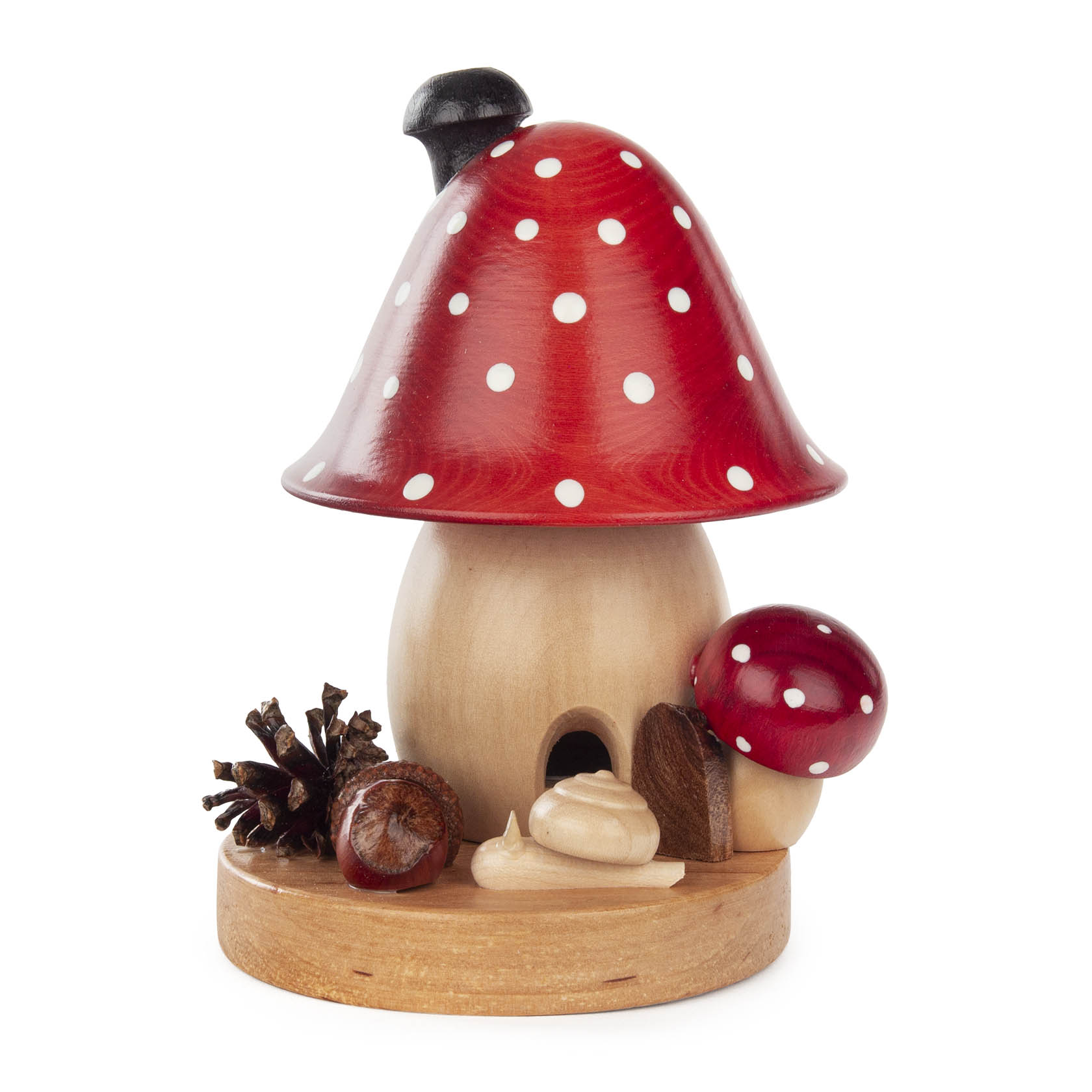 Ein großer Räucherpilz in Form eines Fliegenpilzes mit rotem Hut und weißen Punkten sowie schwarzem Schornstein. Daneben stehen ein kleiner Pilz, eine Kastanie und ein Tannenzapfen auf einem Holzsockel. im Dregeno Online Shop günstig kaufen