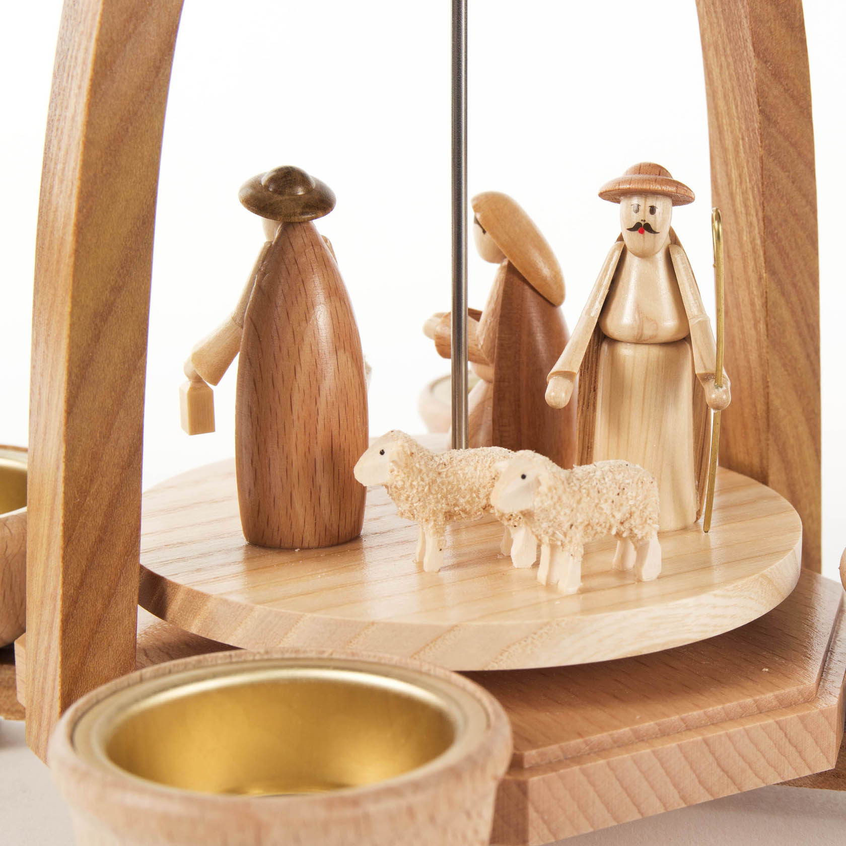 Wooden Christmas pyramid depicting the Nativity scene with hand-carved figures of Mary, Joseph, shepherds, and two sheep, surrounded by tealight holders.